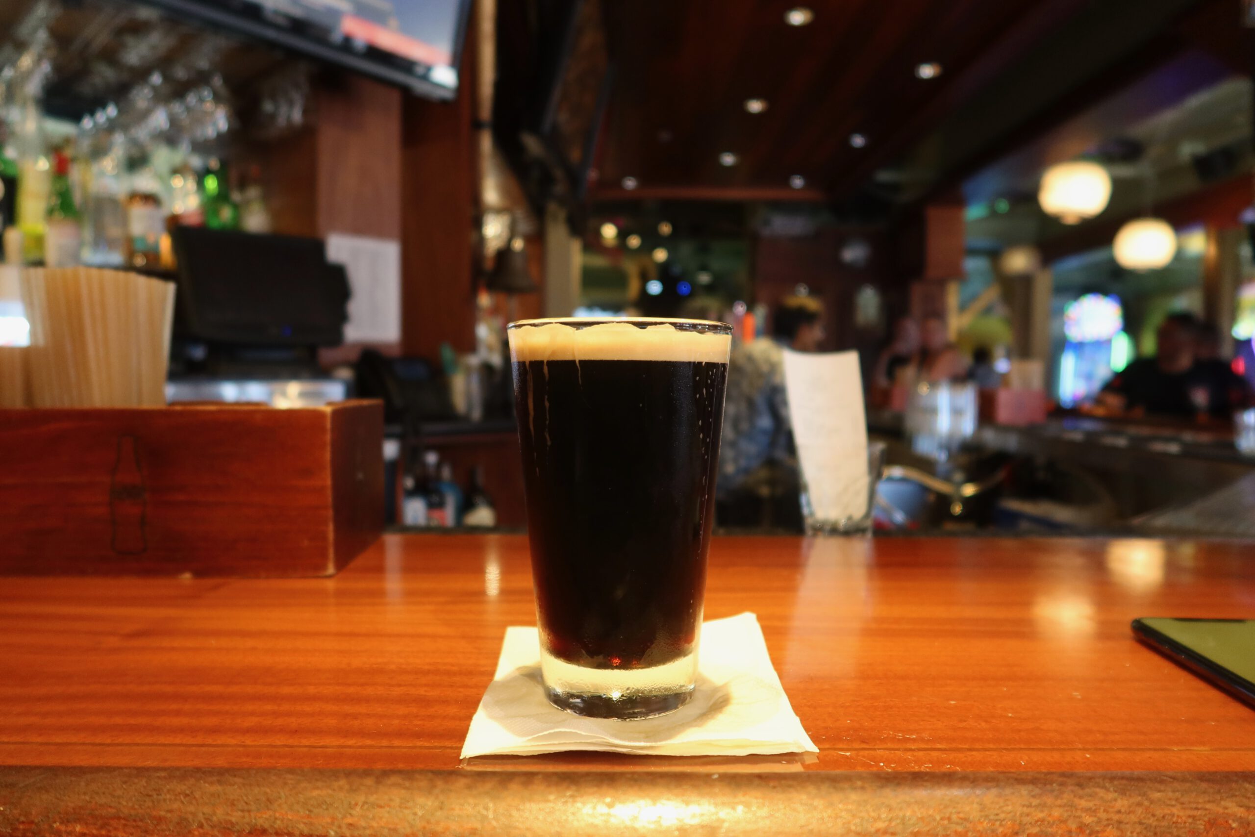 Dark craft beer served at the bar inside Players Sports Grill & Arcade on Pier 39 in San Francisco, shown on a wooden counter with a lively American sports bar background.