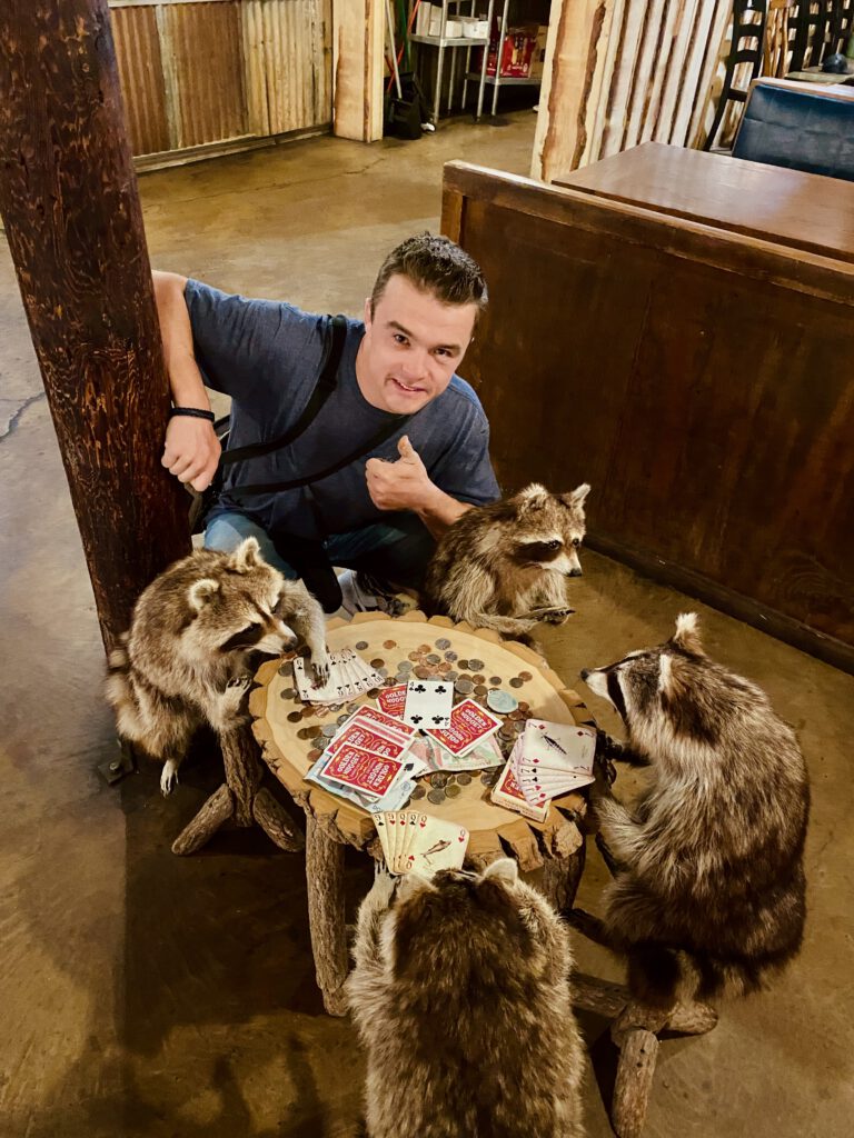 Playful western themed interior at Iron Horse Kanab Utah with a guest posing next to raccoon statues playing cards, showcasing the fun Old West decor.