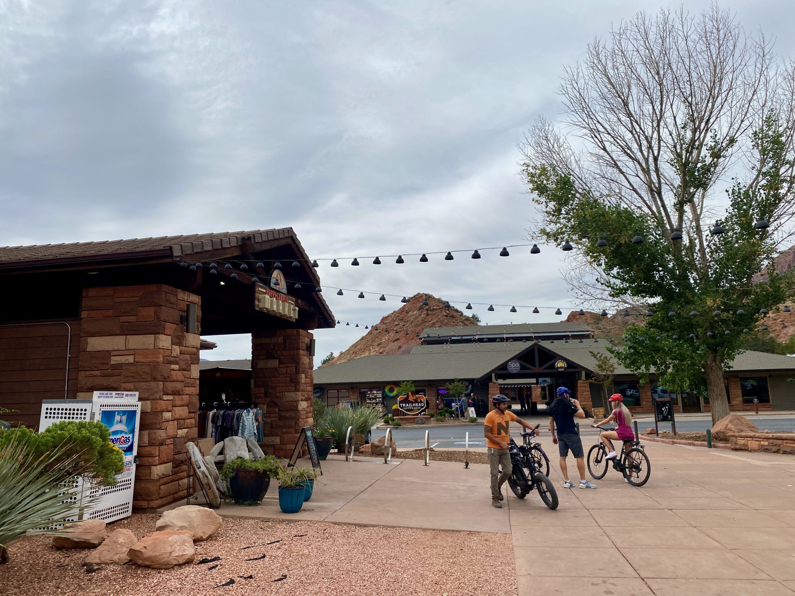 Visitors and cyclists in Springdale near Zion National Park, surrounded by red rock hills, outdoor stores, and desert landscaping