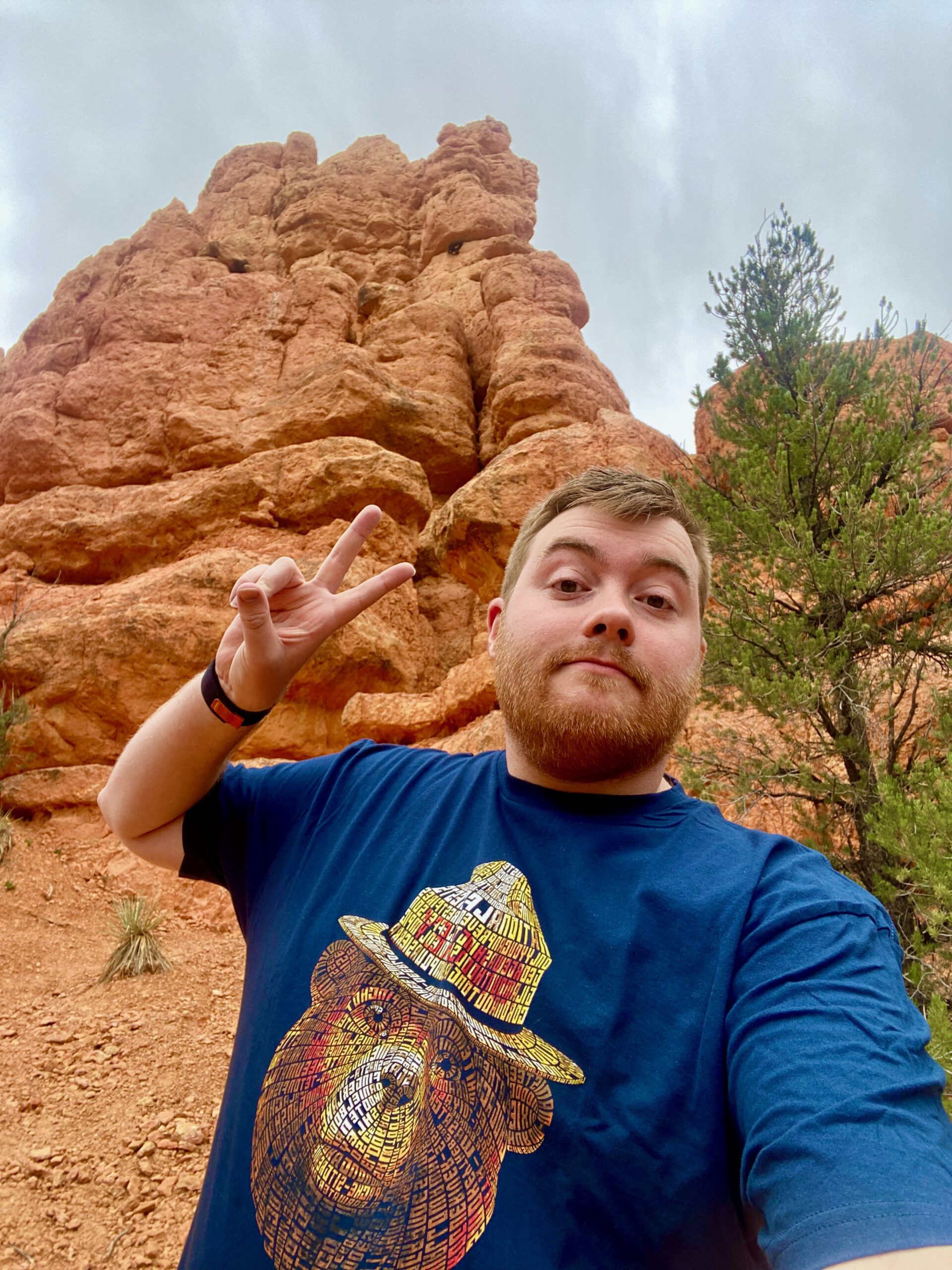 Timo van den Berg, also known as Timeuw, taking a selfie in front of red rock formations in Dixie National Forest, Utah, wearing a Smokey Bear shirt near Red Canyon along Scenic Byway 12