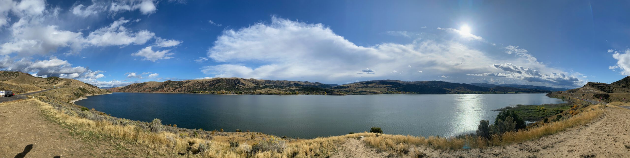 Panoramic view over Echo Reservoir near Coalville Utah, showing calm blue water surrounded by rolling hills and dramatic clouds, photographed from the roadside viewing point along Interstate 80 during a Utah road trip.
