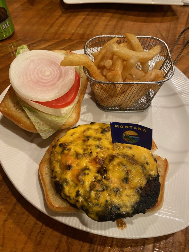 Close-up of a cheeseburger topped with melted cheddar and Cowboy’s Lodge and Grill flag in Gardiner, MT.