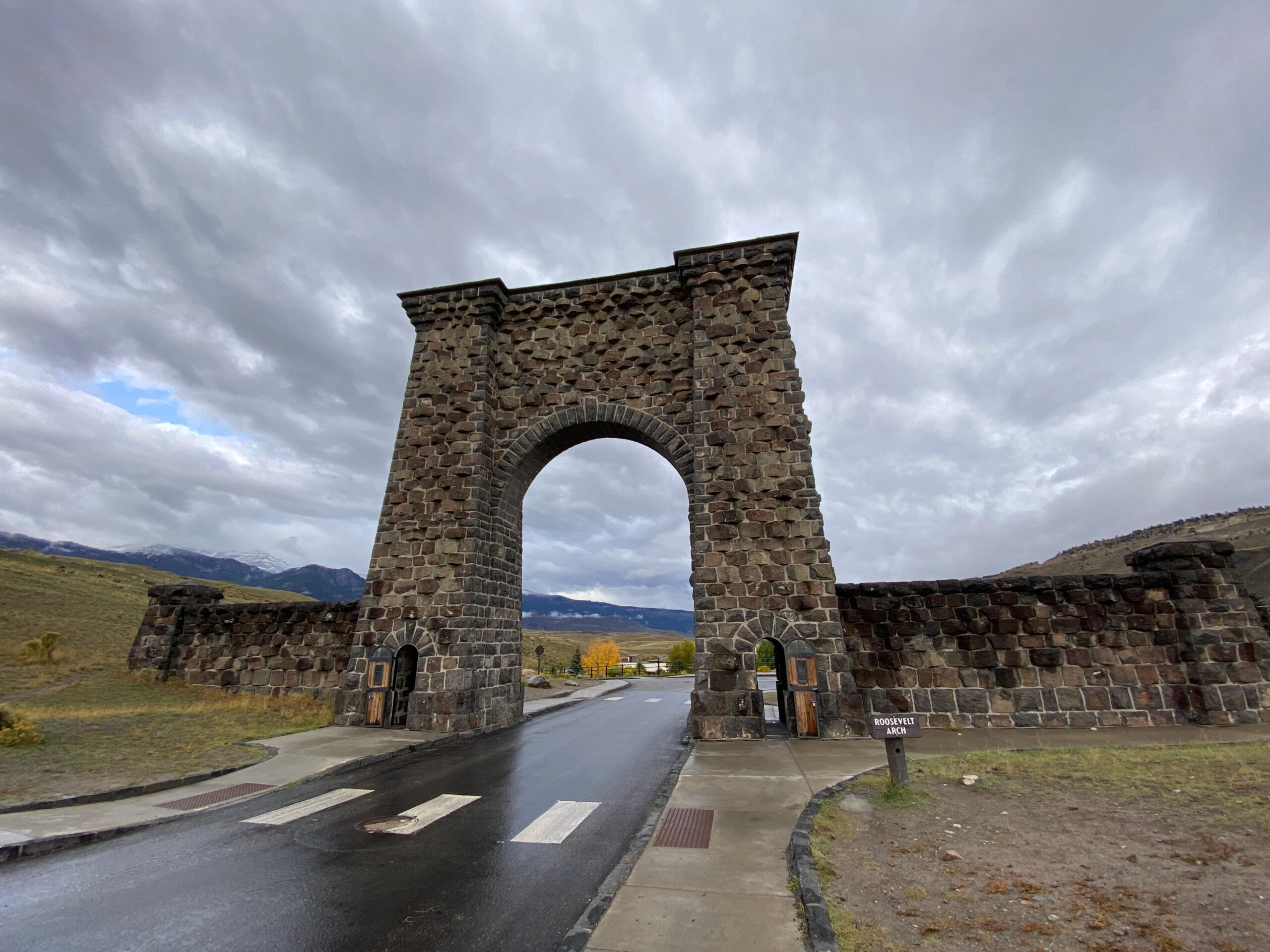 Roosevelt Arch at the Yellowstone North Entrance in Gardiner Montana, historic stone gateway under dramatic cloudy sky