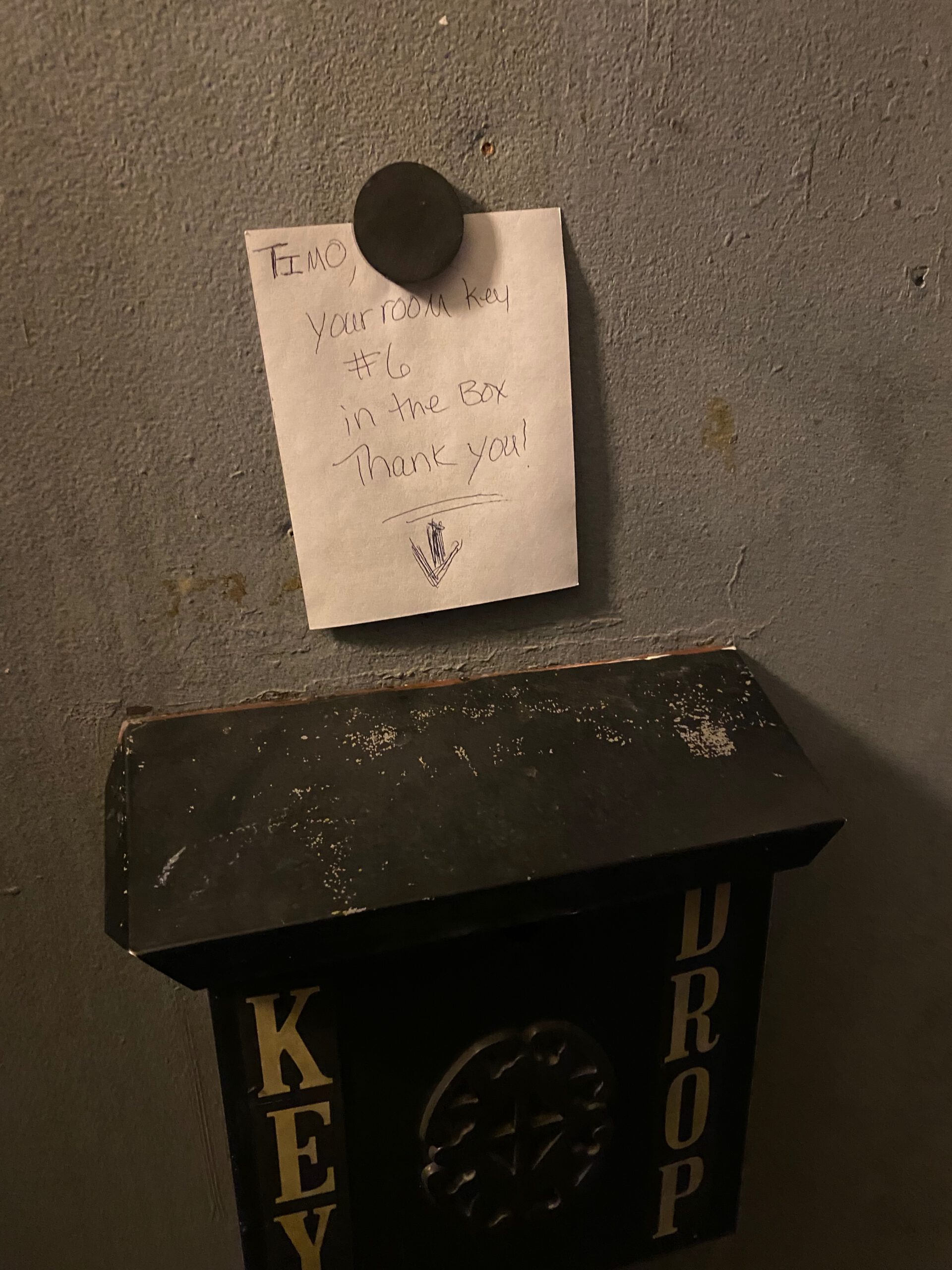 Handwritten welcome note above a key drop box at Arco Inn Motel in Idaho, explaining that the room key is available for late check in, showing a classic self service American motel arrival setup