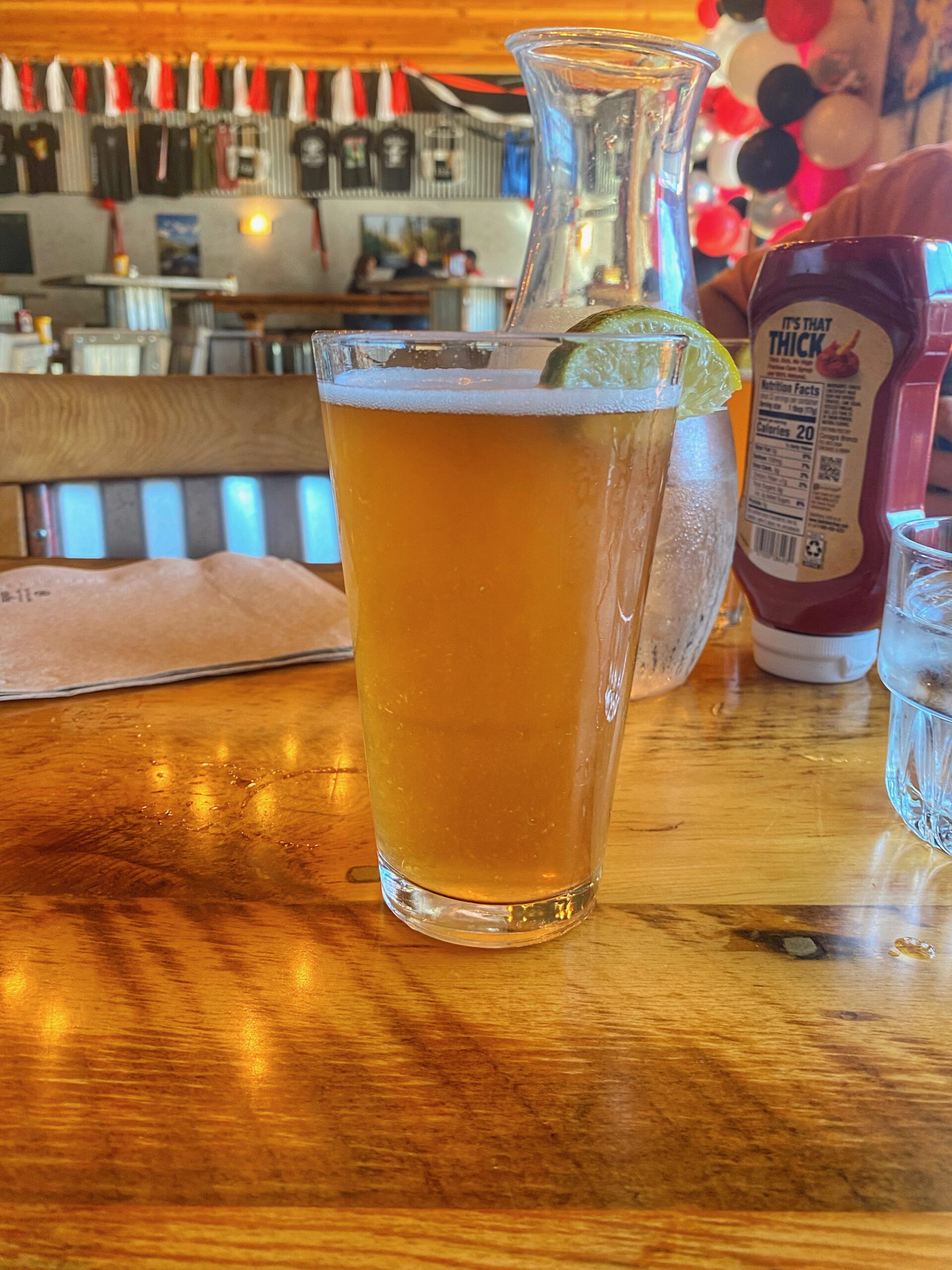 Freshly poured golden craft beer on a wooden table at 1188 Brewing Company in John Day Oregon, showing the relaxed brewery atmosphere with warm lighting and community seating in the background.