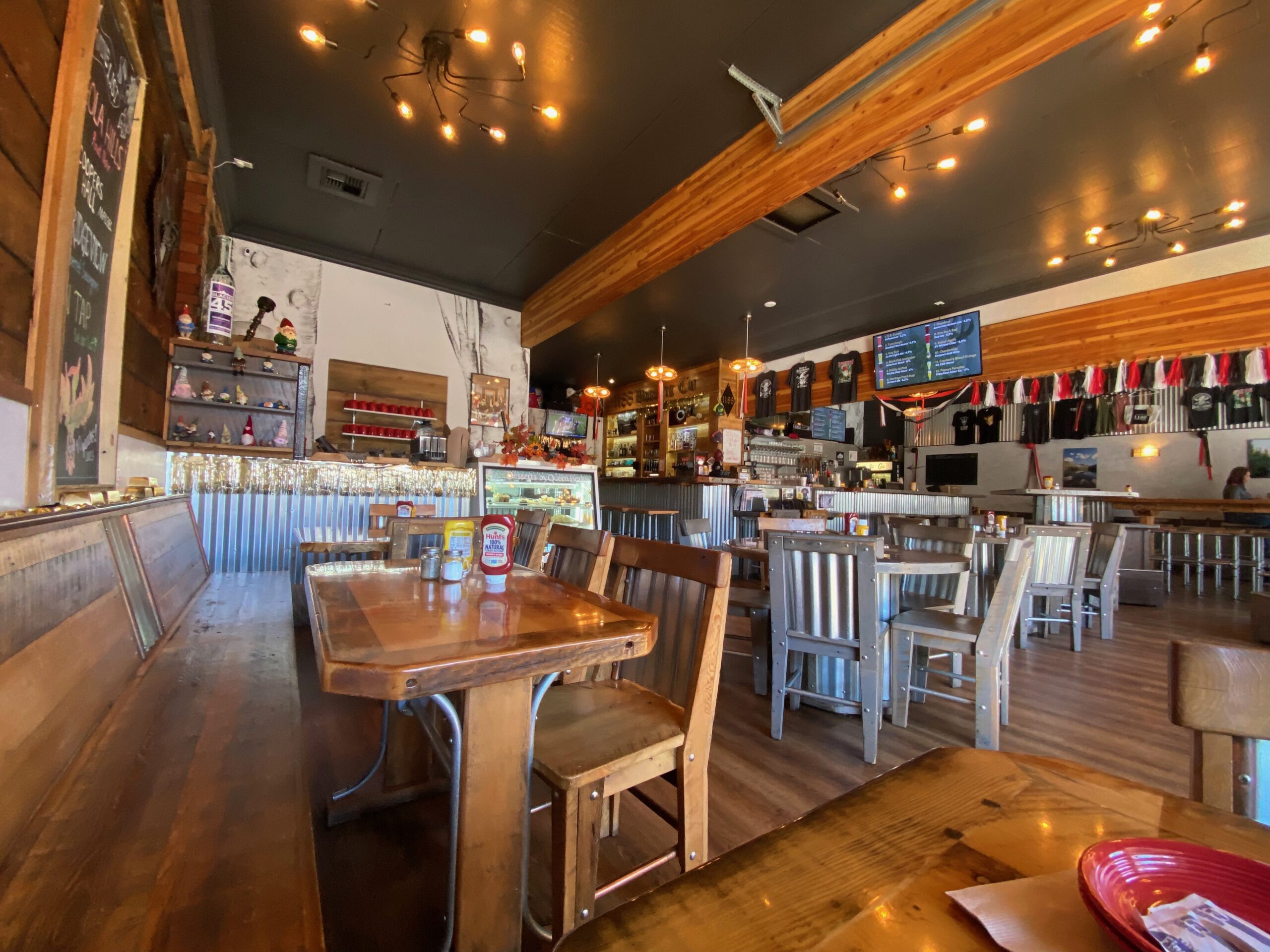 Wide interior view of 1188 Brewing Company in John Day Oregon, featuring rustic wooden tables, metal accents, warm lighting, and a relaxed small town brewery atmosphere with the bar and tap list visible in the background.