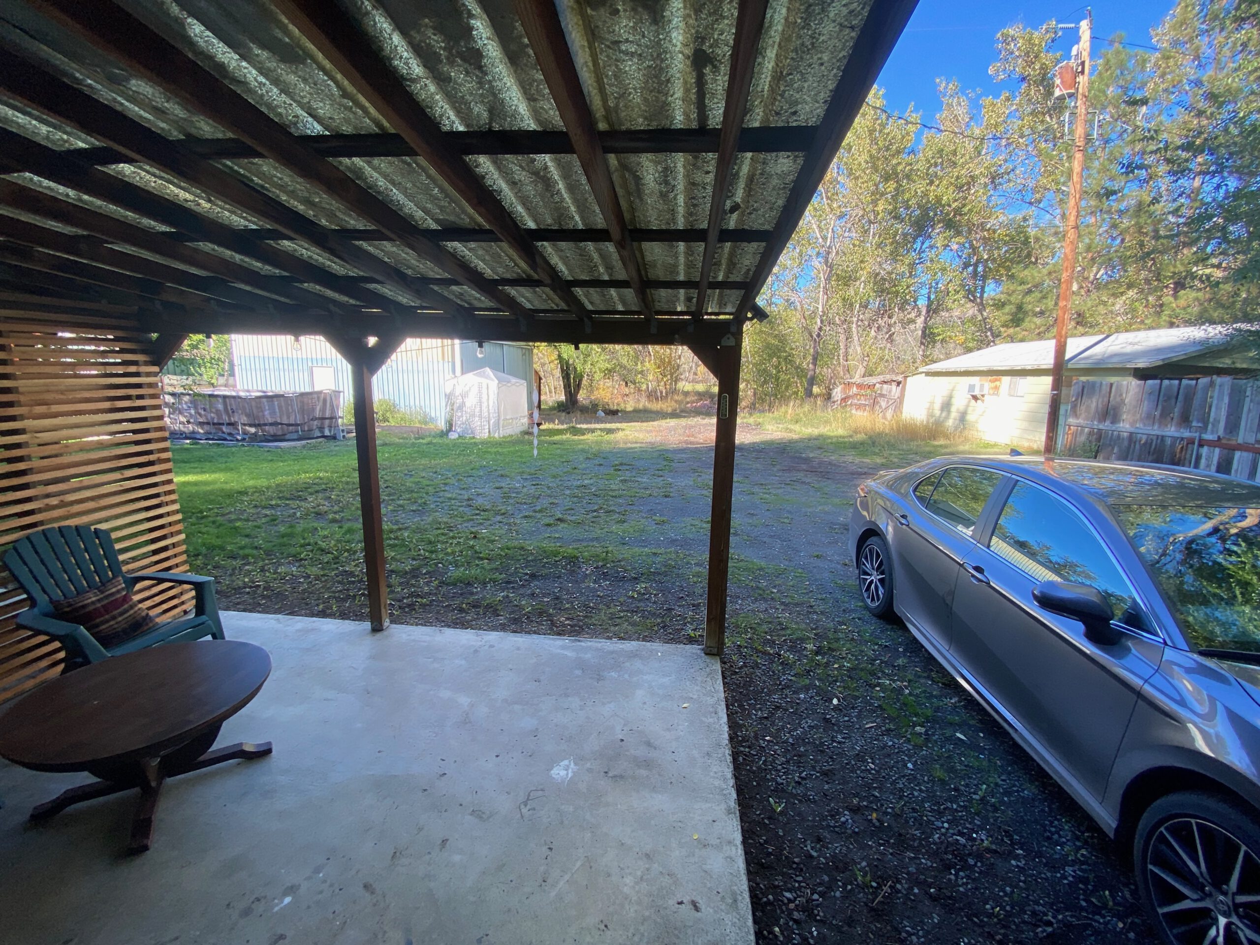 Covered patio at the John Day Airbnb with outdoor seating, looking out over a grassy yard, while a silver Toyota Camry 2024 is parked directly next to the house on a quiet rural property.