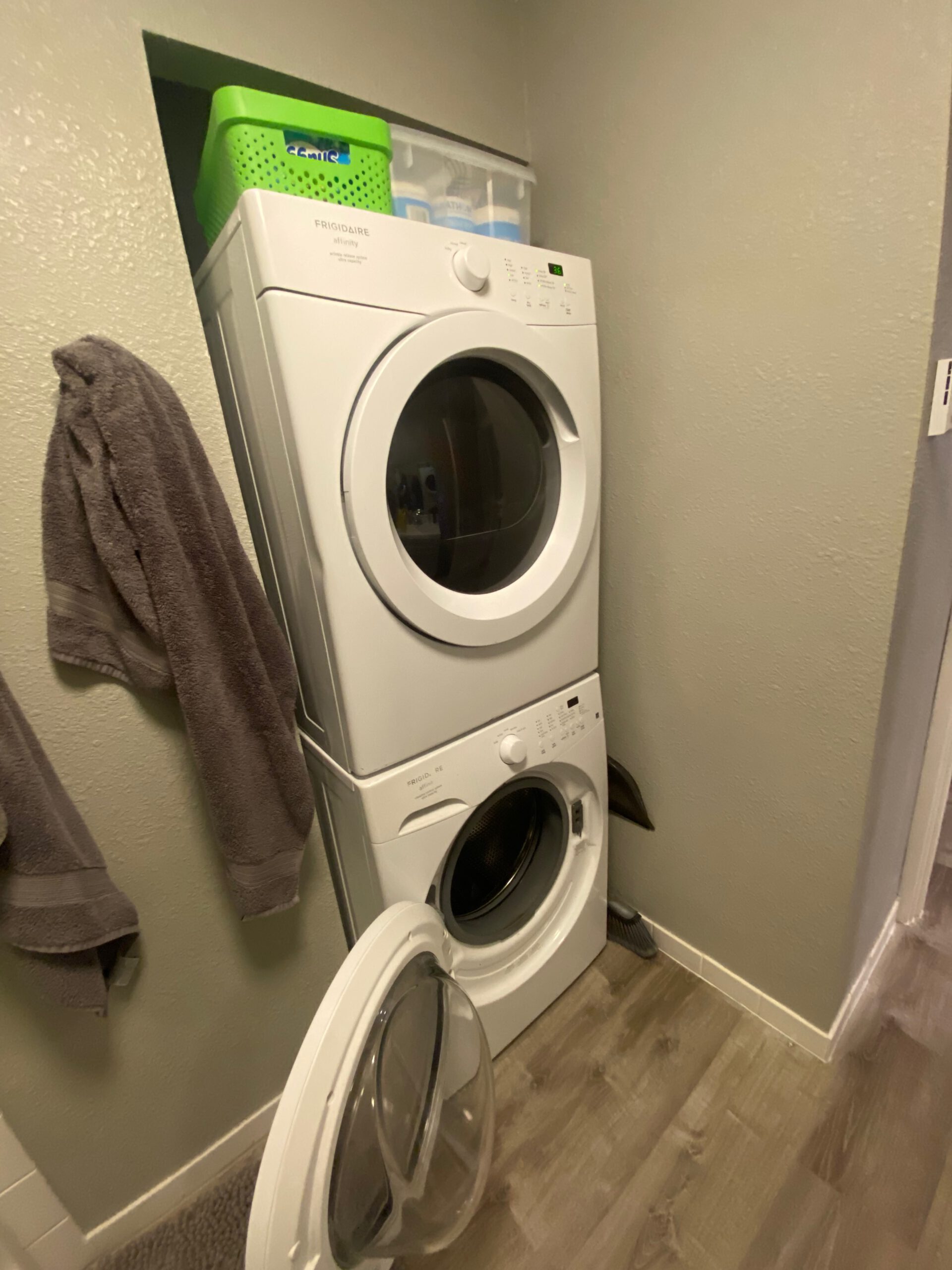 Stacked washer and dryer inside the Airbnb John Day Oregon, located in a small laundry area with towels hanging on the wall and storage bins placed above the machines.