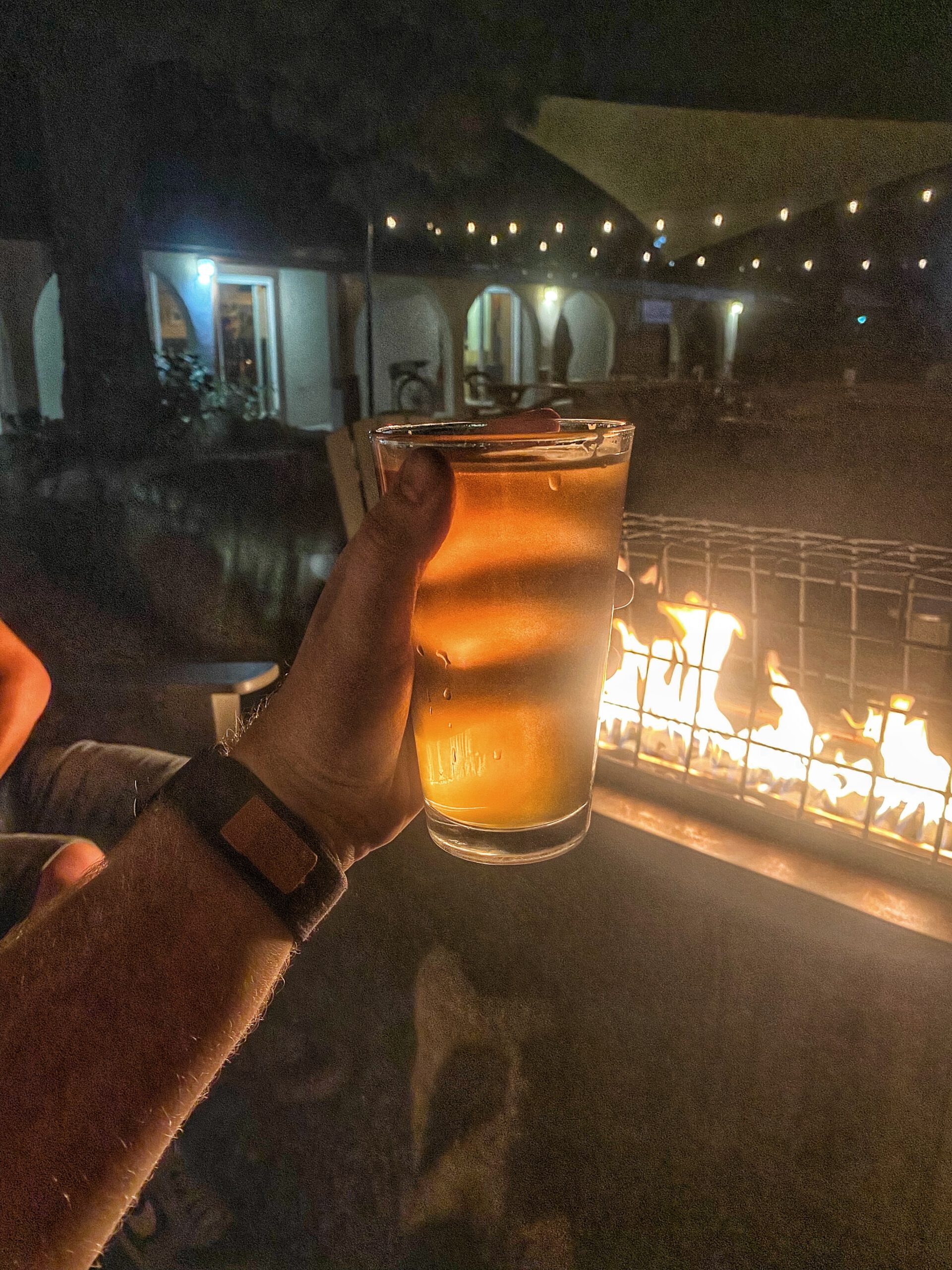 Golden craft beer held near a fire pit at Bear Belly Brewing Company in Kings Beach California, capturing the cozy nighttime atmosphere of a Lake Tahoe outdoor brewery