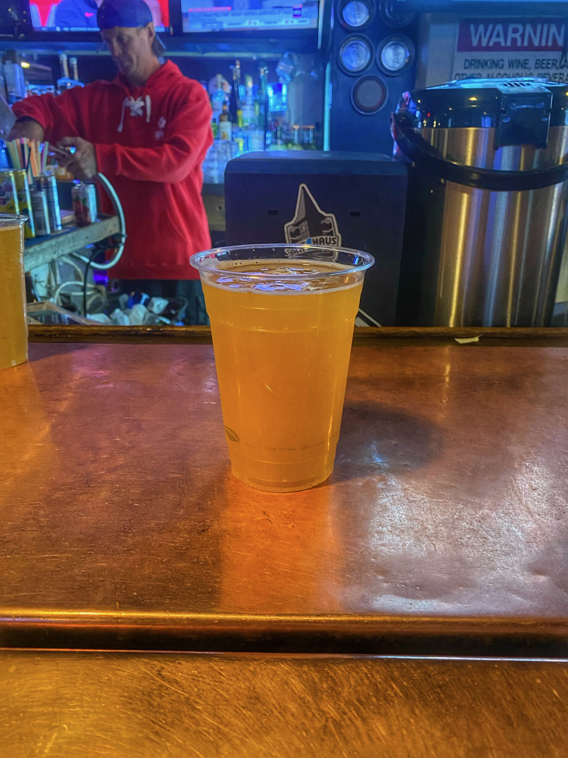 Fresh draft beer served in a plastic cup at a Lake Tahoe bar, with a bartender in the background and a lively evening atmosphere in Kings Beach.