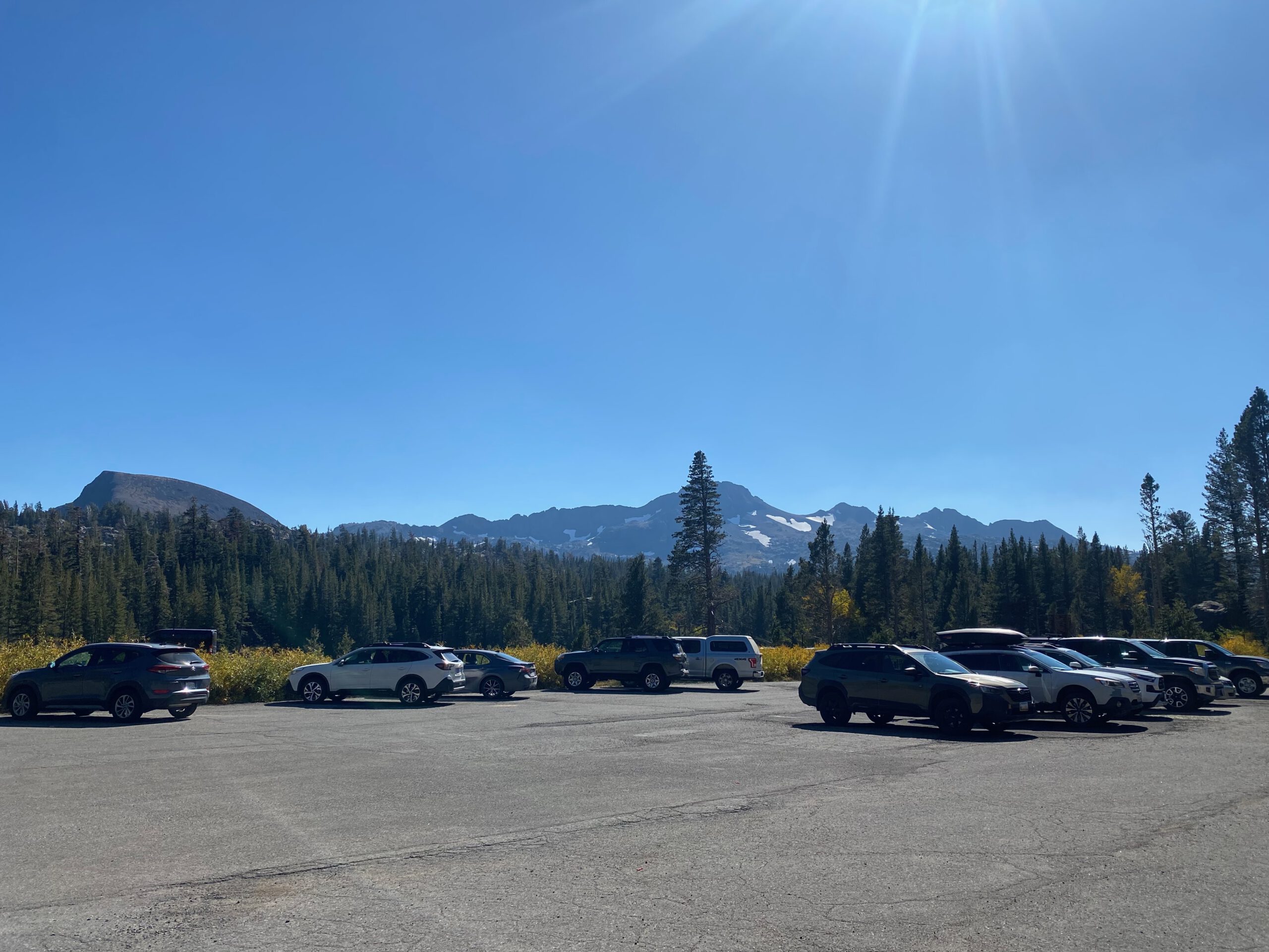 Parking area near Emerald Bay State Park with cars, pine forest, and Sierra Nevada mountain peaks under a clear blue sky at Lake Tahoe, California.