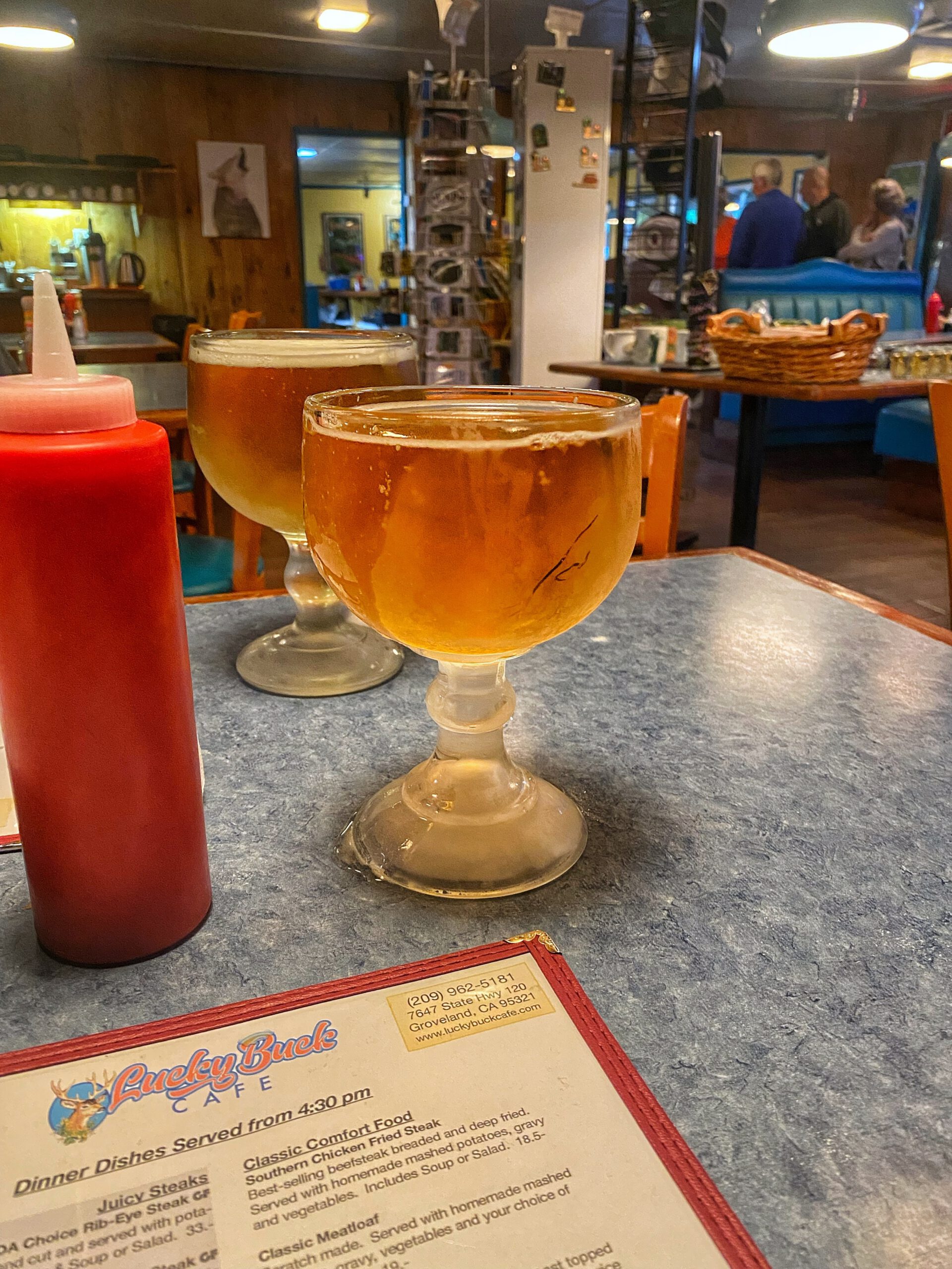 Cold draft beers served in frosted glasses on a diner table at Lucky Buck Cafe California, with classic condiment bottle and printed menu visible inside a traditional American diner near Yosemite.