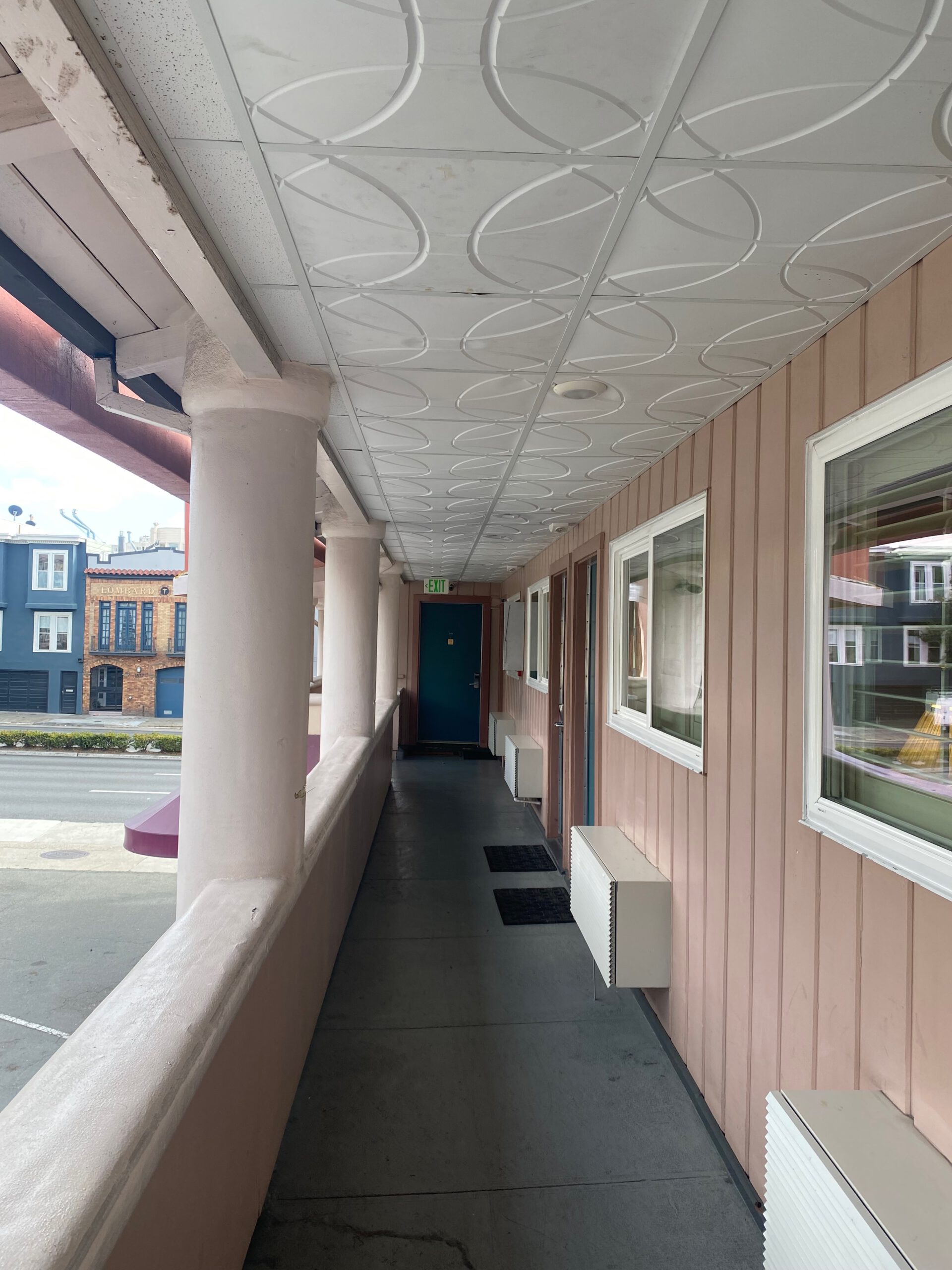 Exterior motel hallway at Town House Motel in San Francisco with pastel pink walls, teal room doors, white columns and classic mid-century ceiling details