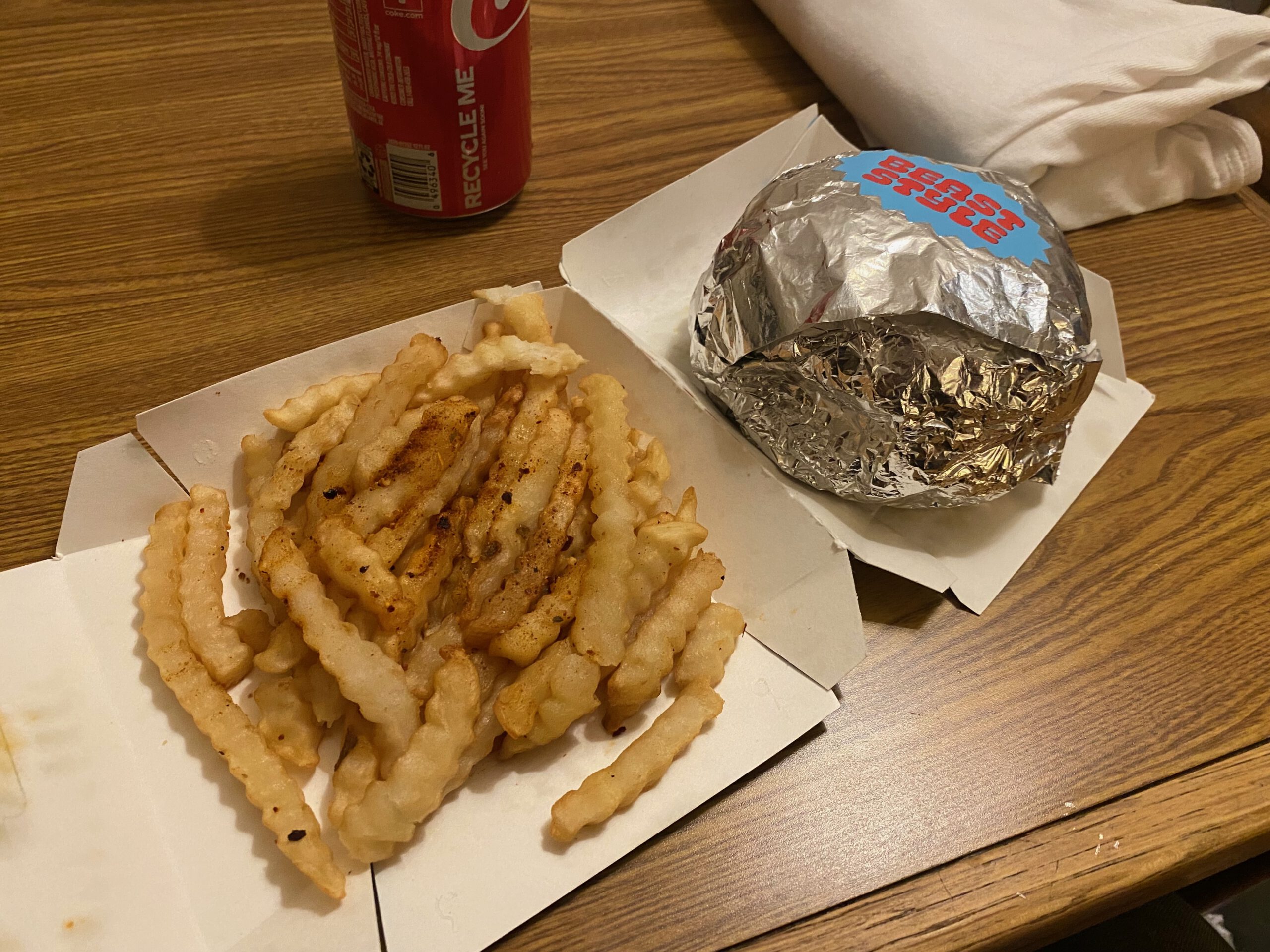 Late night fast food meal in San Francisco motel room, crinkle cut fries and wrapped burger on wooden table, simple American takeout of MrBeast Burger San Fransisco during city stay