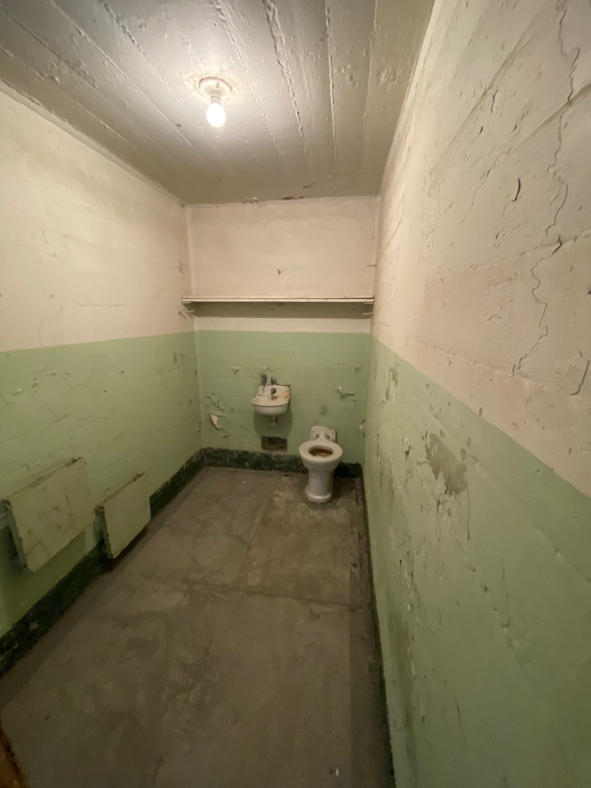 Empty prison cell on Alcatraz Island with original toilet, sink and peeling green walls inside the historic Cell House