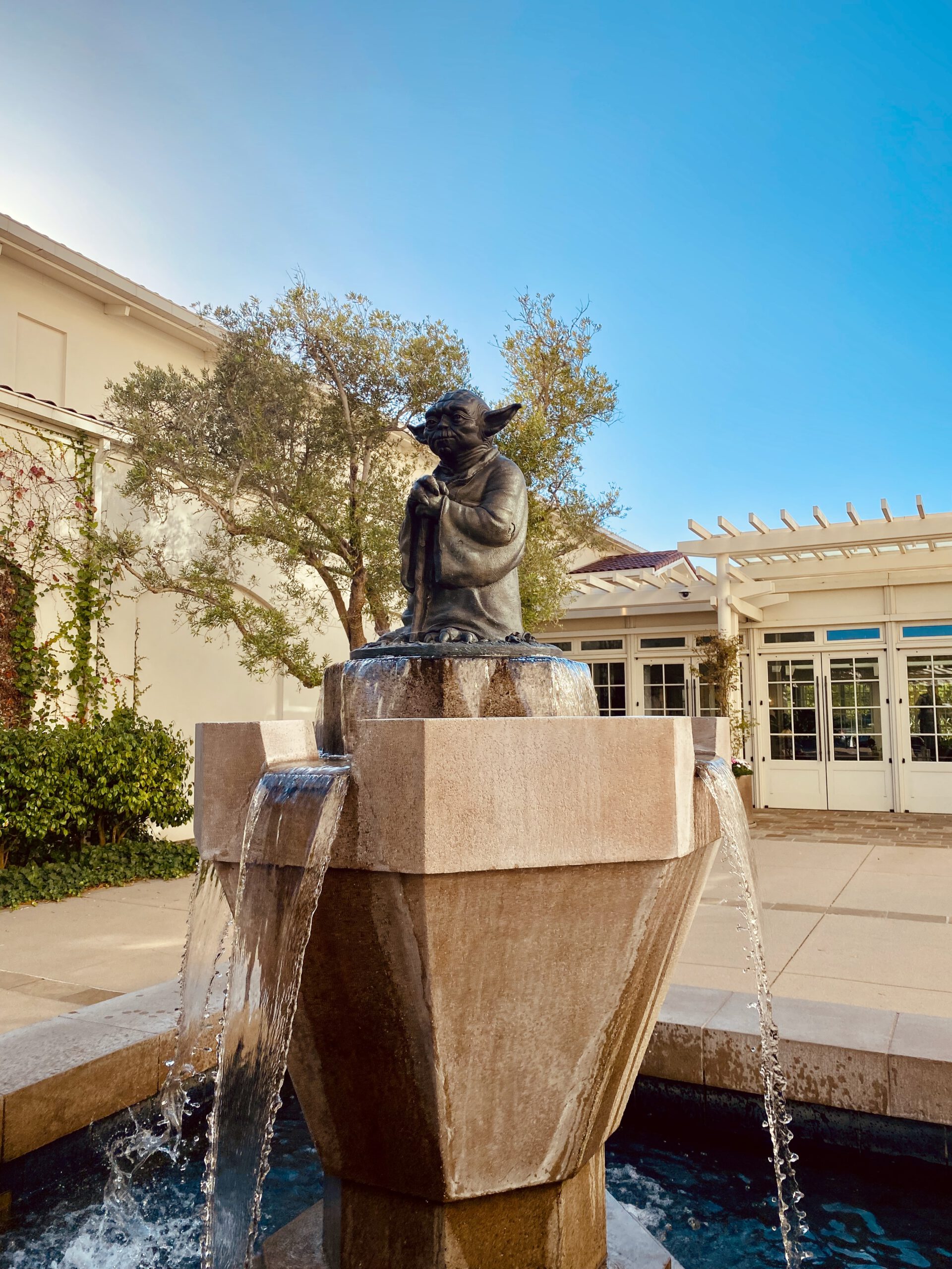 Yoda Fountain San Francisco in the Presidio, bronze Yoda statue standing on a geometric stone fountain with flowing water and clear blue sky
