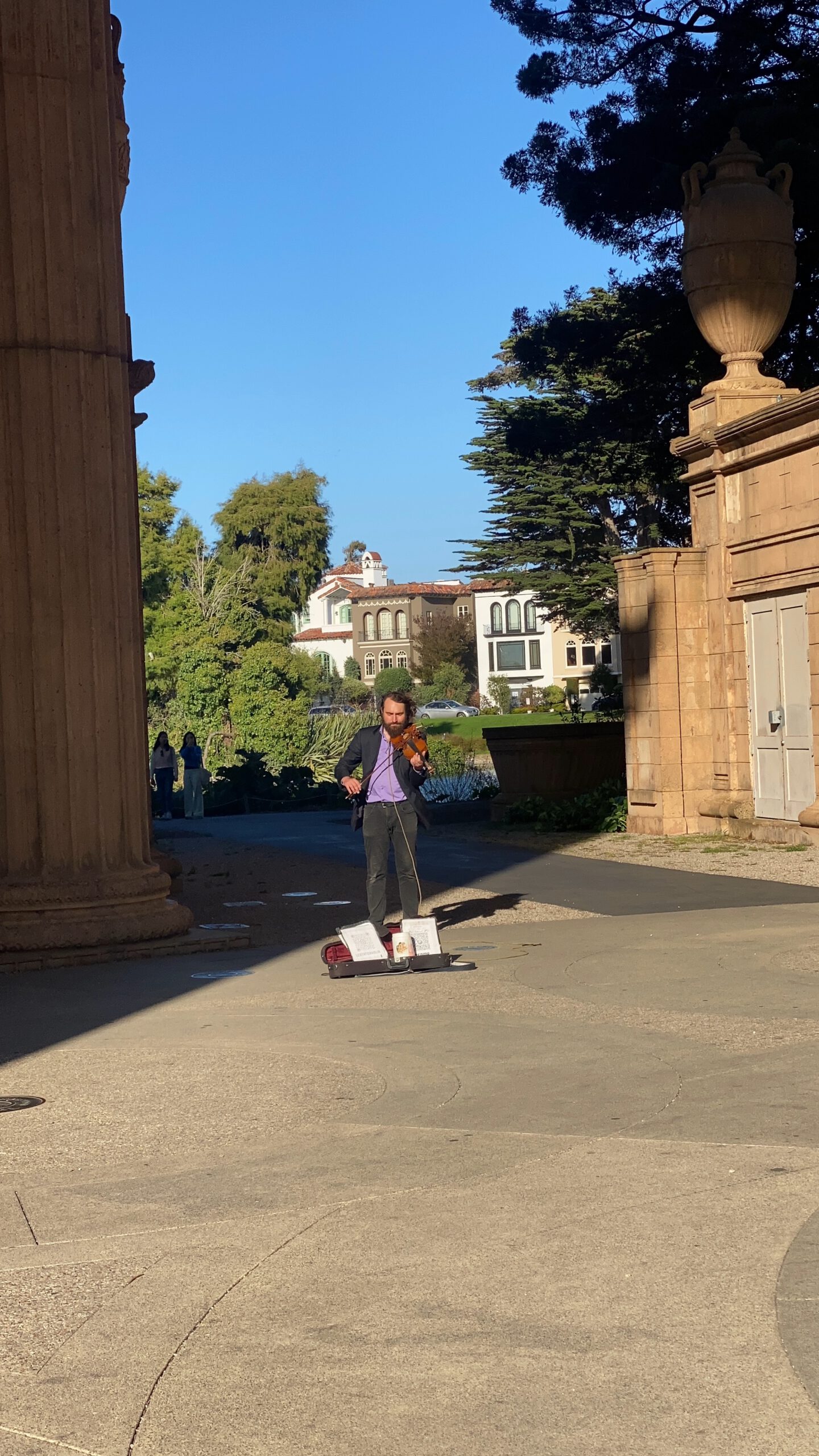 Street musician performing violin music beneath the Palace of Fine Arts San Francisco rotunda, creating a calm and atmospheric moment framed by classical columns and warm afternoon light