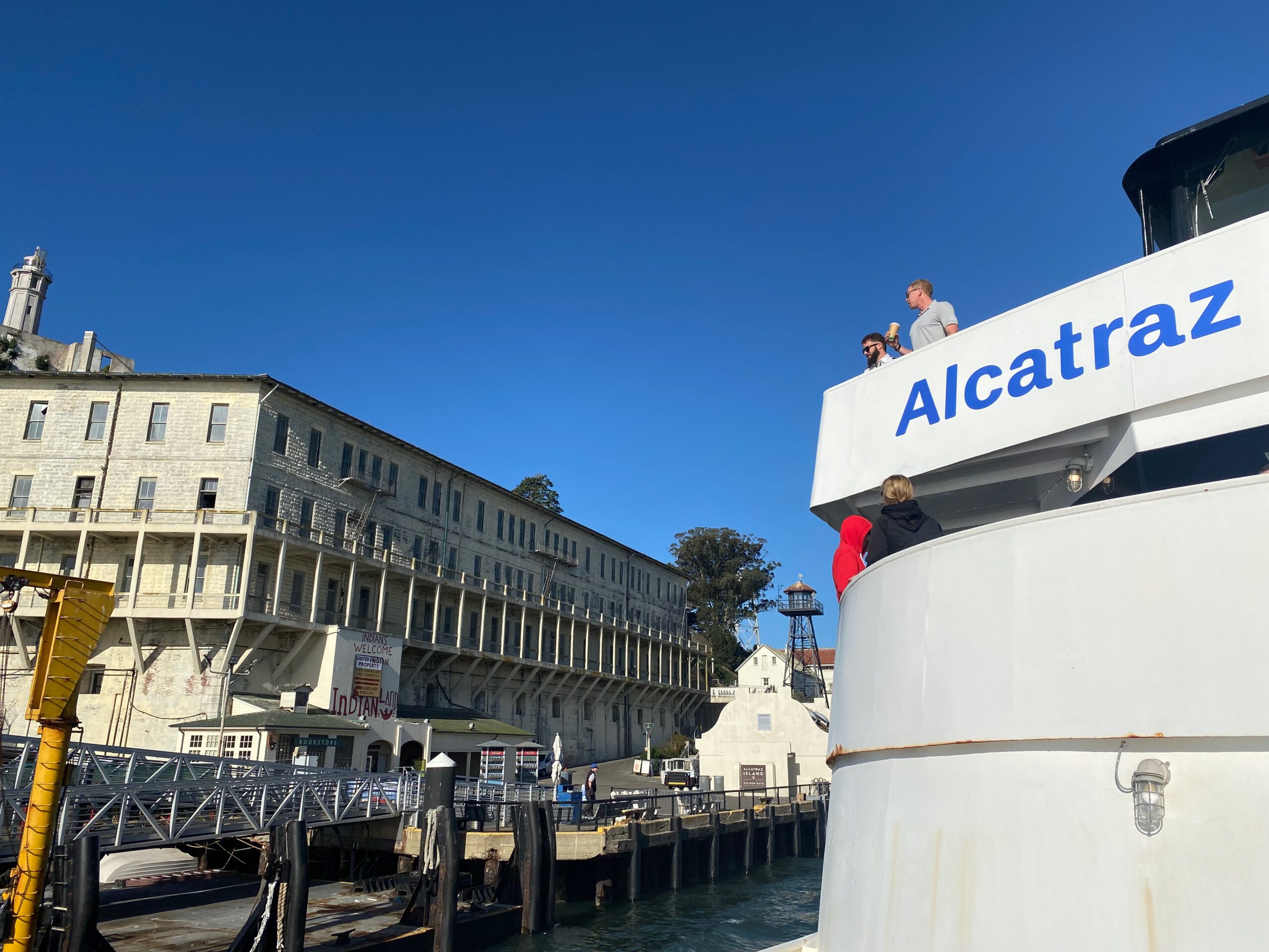 Arriving at Alcatraz Island by ferry with visitors on deck, the main prison building, guard tower and dock visible at Pier 33 landing area