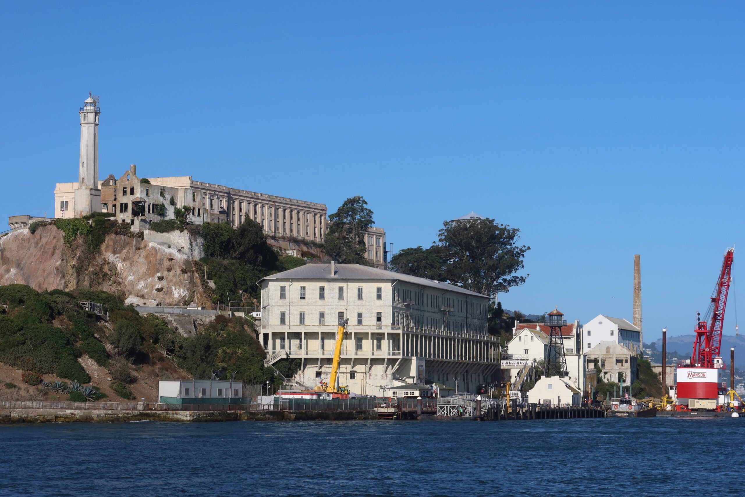 Alcatraz Island viewed from San Francisco Bay with the historic Cell House, lighthouse and harbor buildings under a clear blue sky