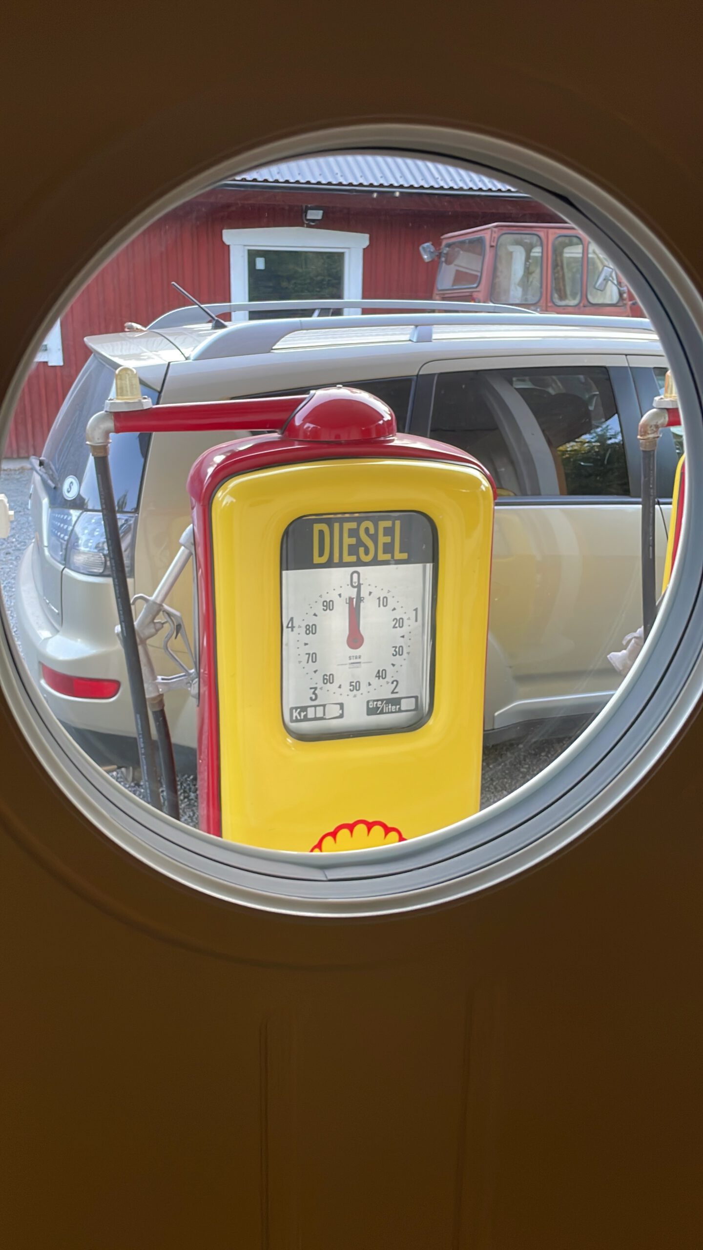 Shell Gas Station Airbnb Enkoping Sweden view through round window showing a vintage Shell diesel fuel pump outside the nostalgic gas station Airbnb
