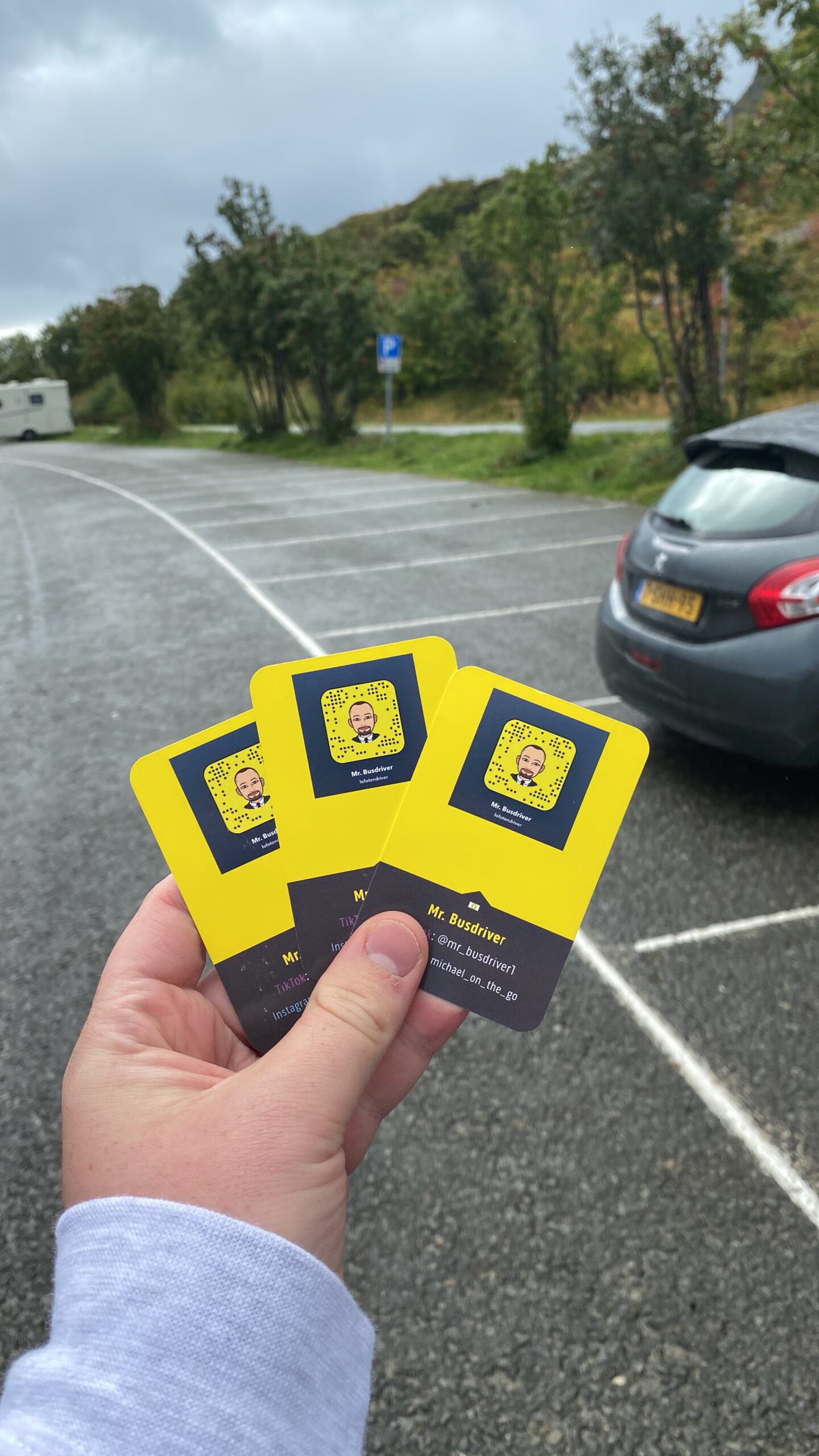 Å Rorbuer Lofoten travel moment with Snapchat cards held in hand at a quiet parking area near Å i Lofoten Norway