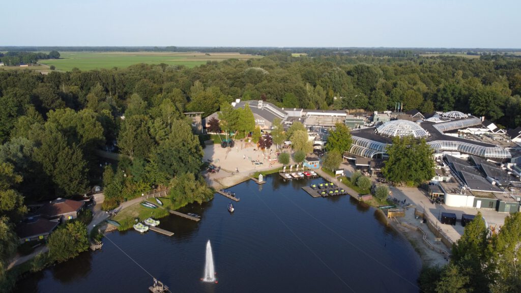 Center Parcs De Huttenheugte Day Visit aerial drone view of the lake, Market Dome with glass dome roof, Aqua Mundo complex, Action Factory and surrounding forest landscape in Dalen, Drenthe during golden hour.