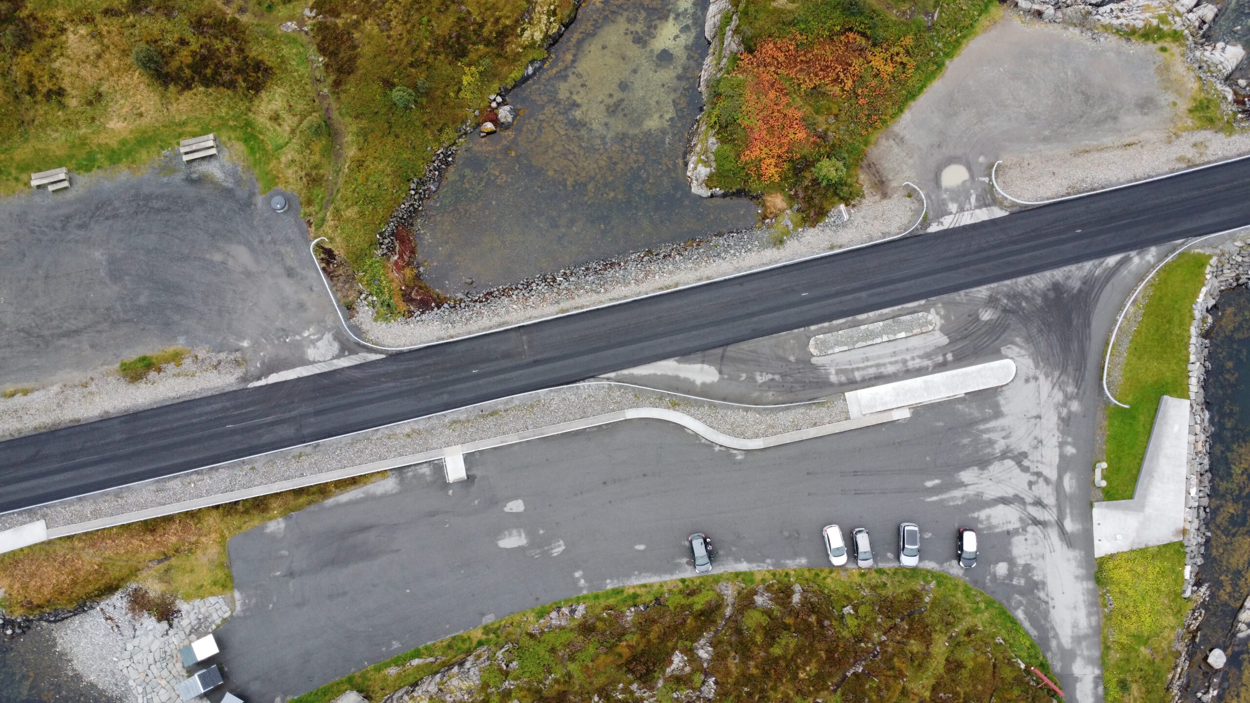 Aerial drone view of Atlantic Ocean Road Norway showing parking area, coastal walking path, County Road 64 bridge section, rocky shoreline, and surrounding islands in Møre og Romsdal