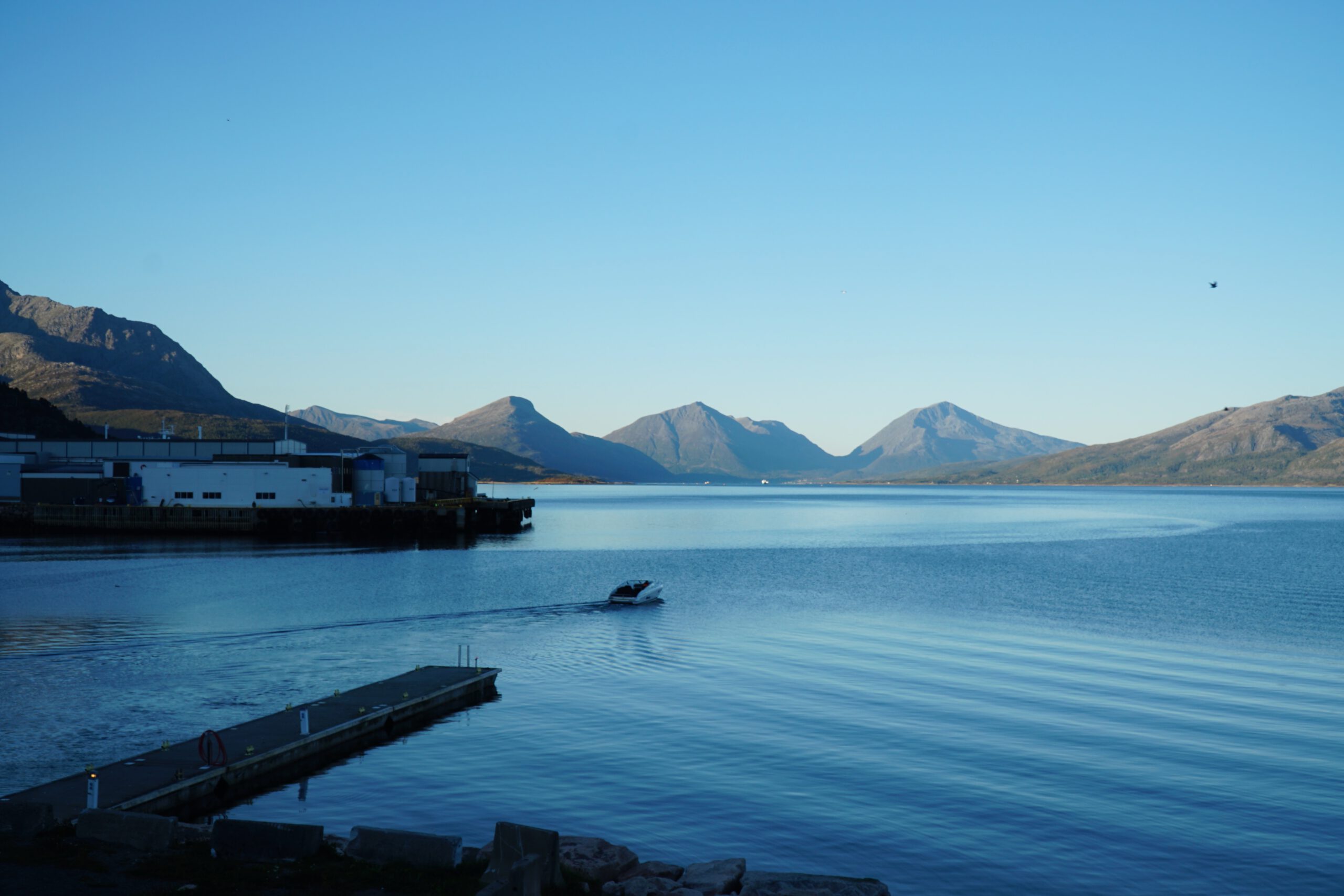Lødingen Brygge Lofoten Norway harbor view with calm blue water, small boat, fjord and mountain landscape under a clear sky