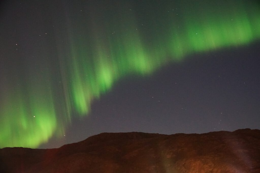 Northern Lights above the mountains near Lødingen Brygge Hotel Norway, green aurora dancing over a dark mountain ridge in Northern Norway