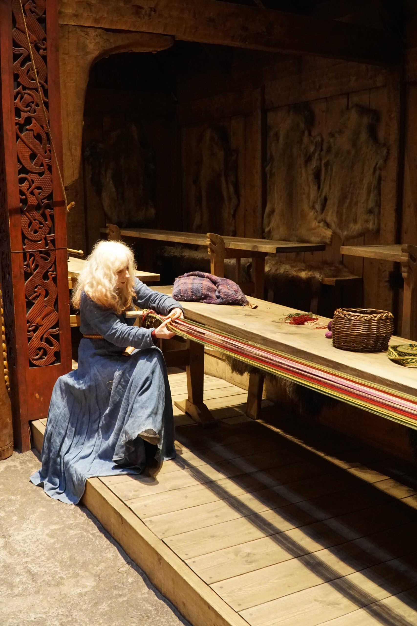 Lofotr Viking Museum reconstructed Viking longhouse interior showing traditional weaving activity with period clothing and wooden tools in Borg, Lofoten Islands