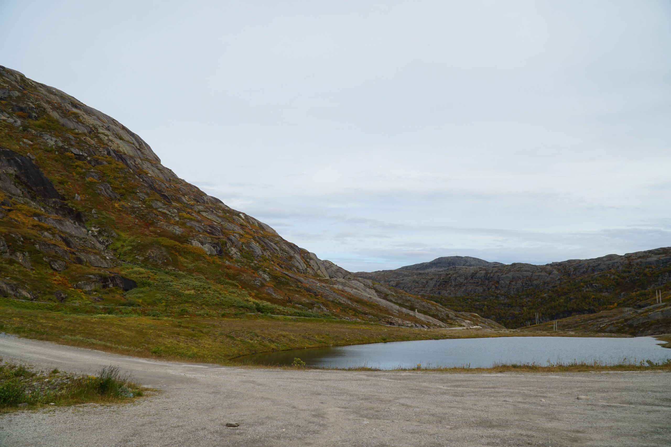 Quiet shoreline of Storglomvatnet with gravel road, calm water, and rugged mountain landscape in northern Norway