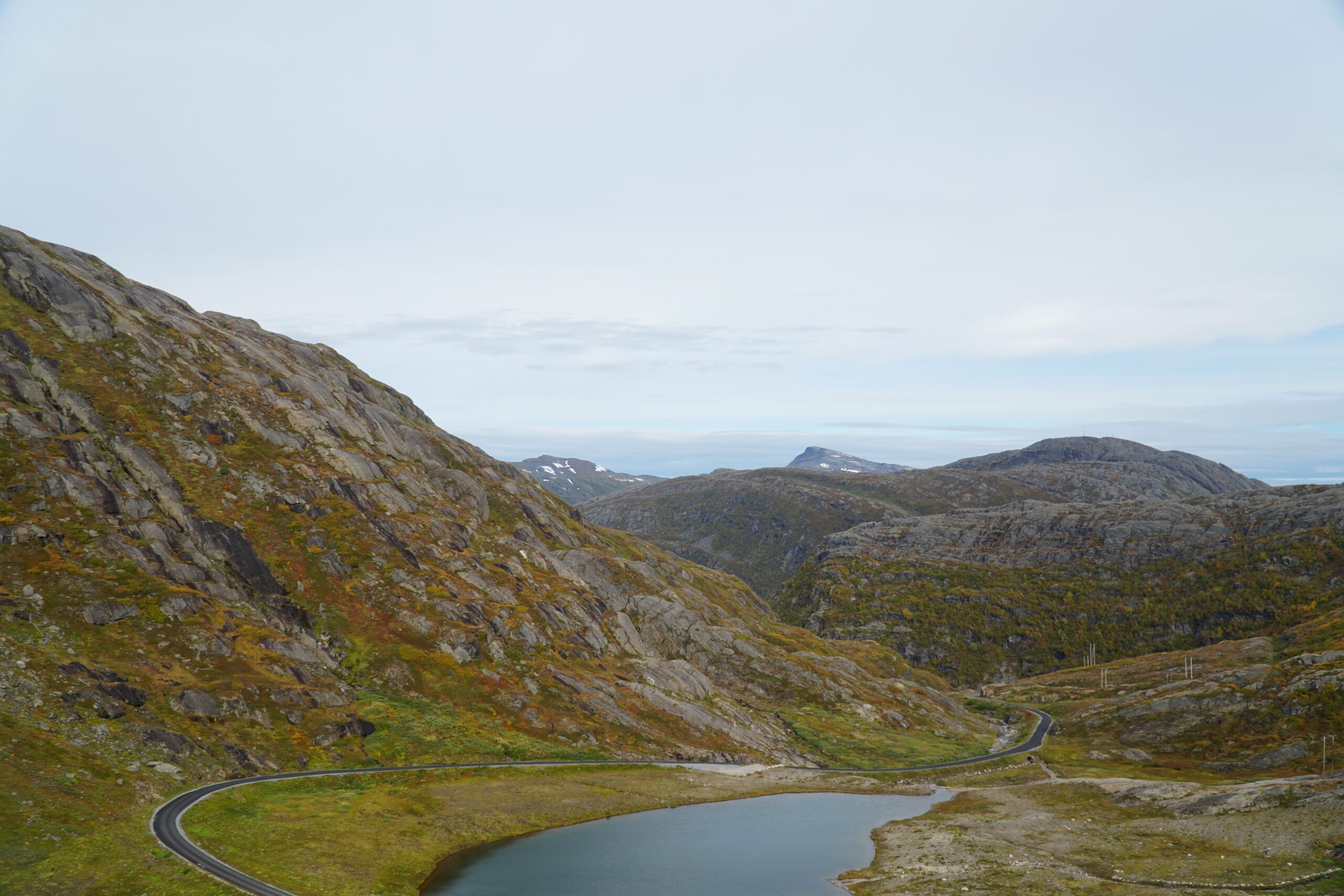 Panoramic view over Storglomvatnet with a winding mountain road, rocky slopes, and colorful Arctic vegetation in the Norwegian highlands