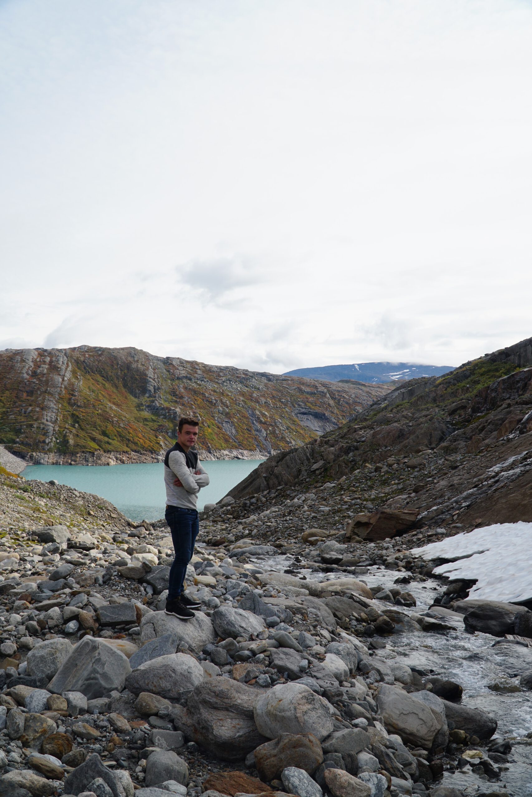 Glomfjord lake and dam adventure with Peter Smit standing on rocky terrain beside Storglomvatnet, surrounded by mountains, snow patches and flowing meltwater in Northern Norway