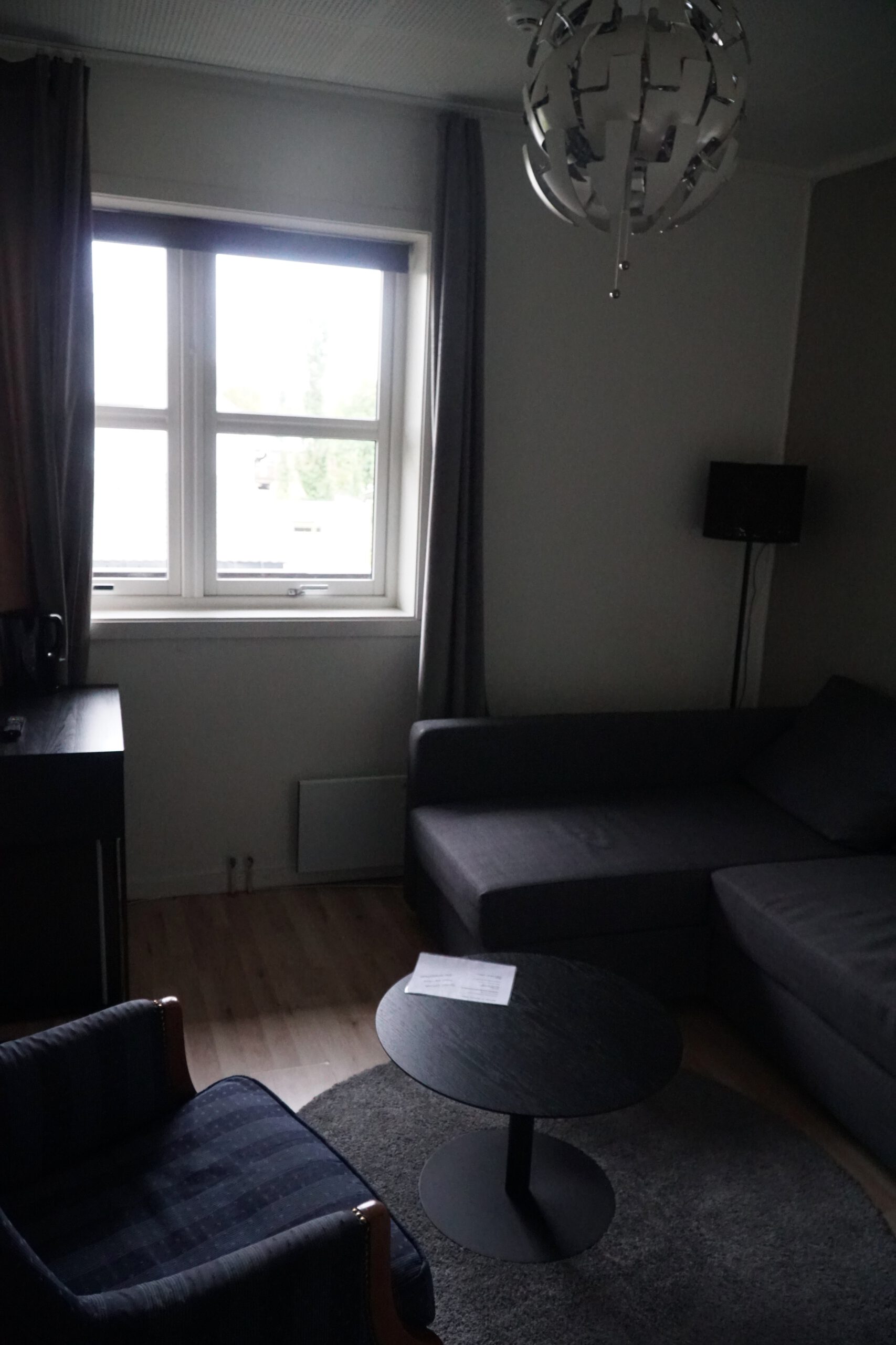 Living area inside Mosjøen Romutleie Sentrum 3 featuring a sofa, armchair, round table, window with curtains, and minimalist interior, a practical budget room setup in Mosjøen, Norway