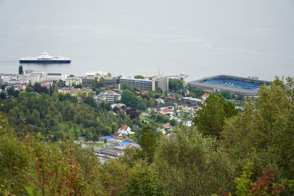 Vardestua Restaurant Molde view over the city center and Molde FK stadium, ferry in the fjord below, colorful houses and forested hillside seen from 407 meters above sea level in Norway.