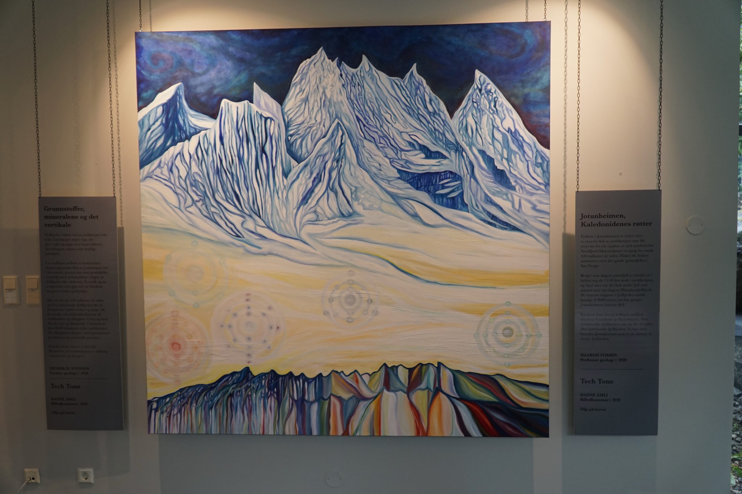Colorful mountain artwork inside Norsk Fjordsenter Geiranger featuring dramatic snow covered peaks, layered rock formations in vibrant tones, and educational panels about Jotunheimen geology