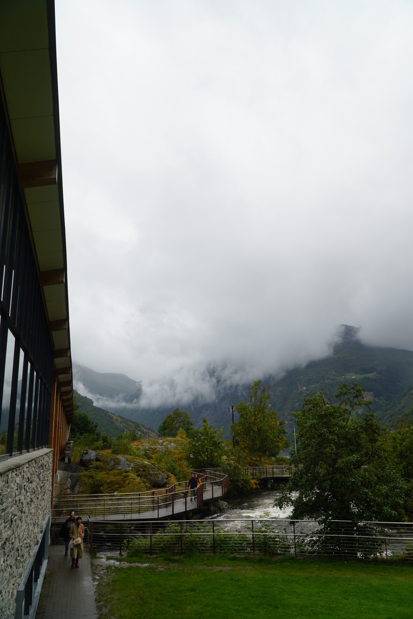Norsk Fjordsenter Geiranger waterfall walkway with visitors near Kleivafossen rapids and mist covered mountains in the Geirangerfjord area