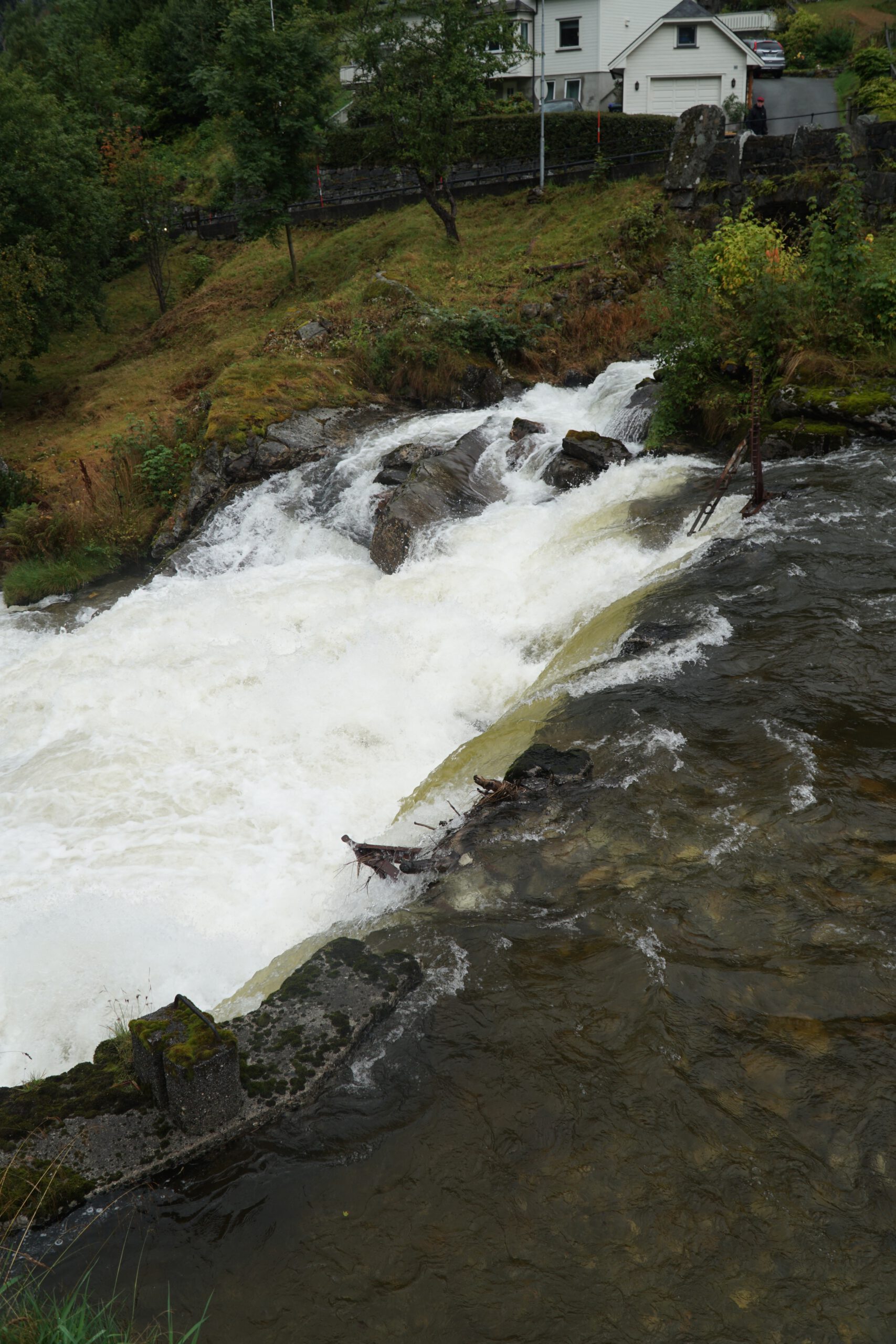 Rushing river and waterfall below Norsk Fjordsenter Geiranger flowing past rocks and hillside houses in the dramatic Geirangerfjord valley