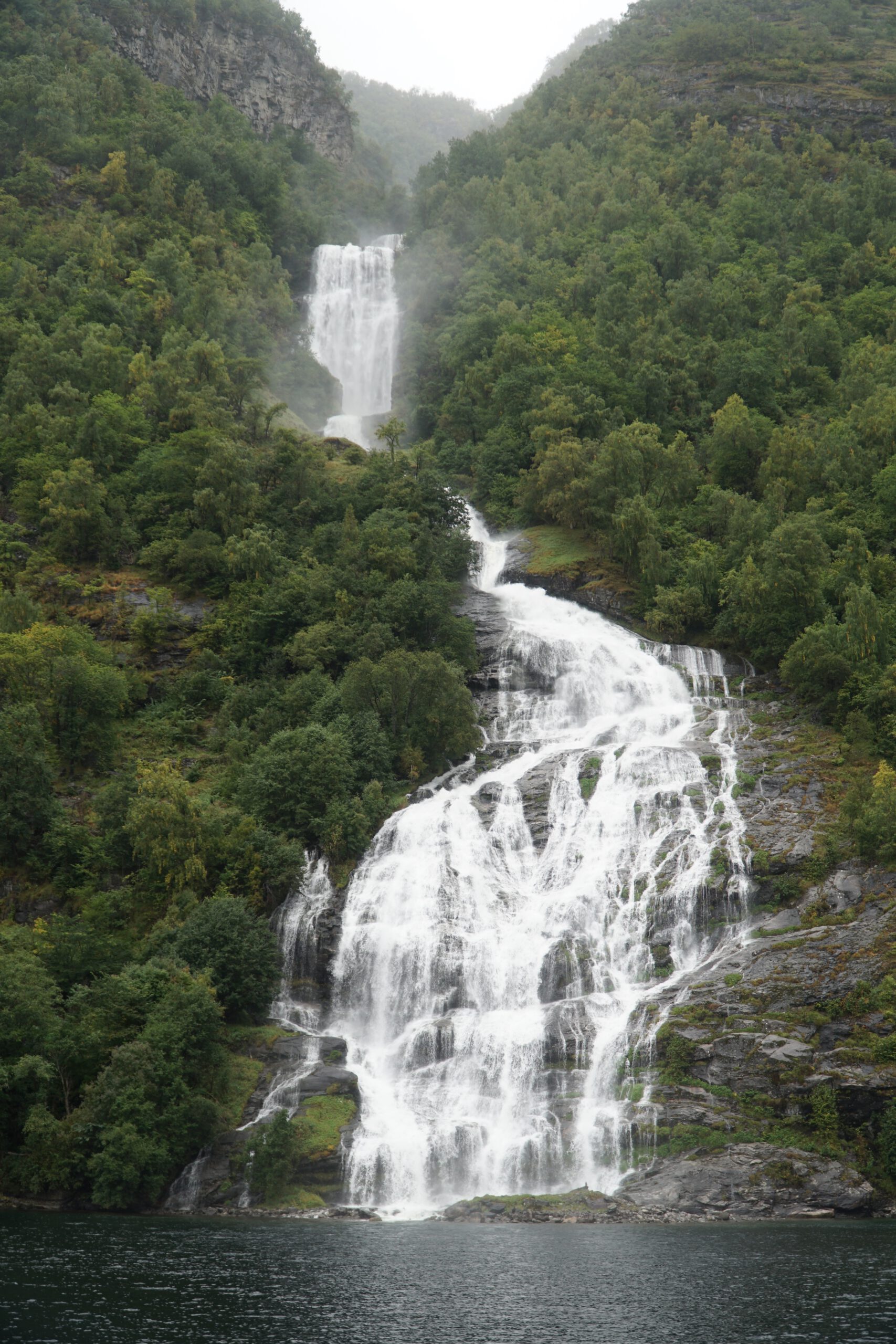 Seven Sisters waterfall cascading into Geirangerfjord during the Geiranger Fjord and Waterfalls Sightseeing Boat Trip surrounded by lush green cliffs and mist