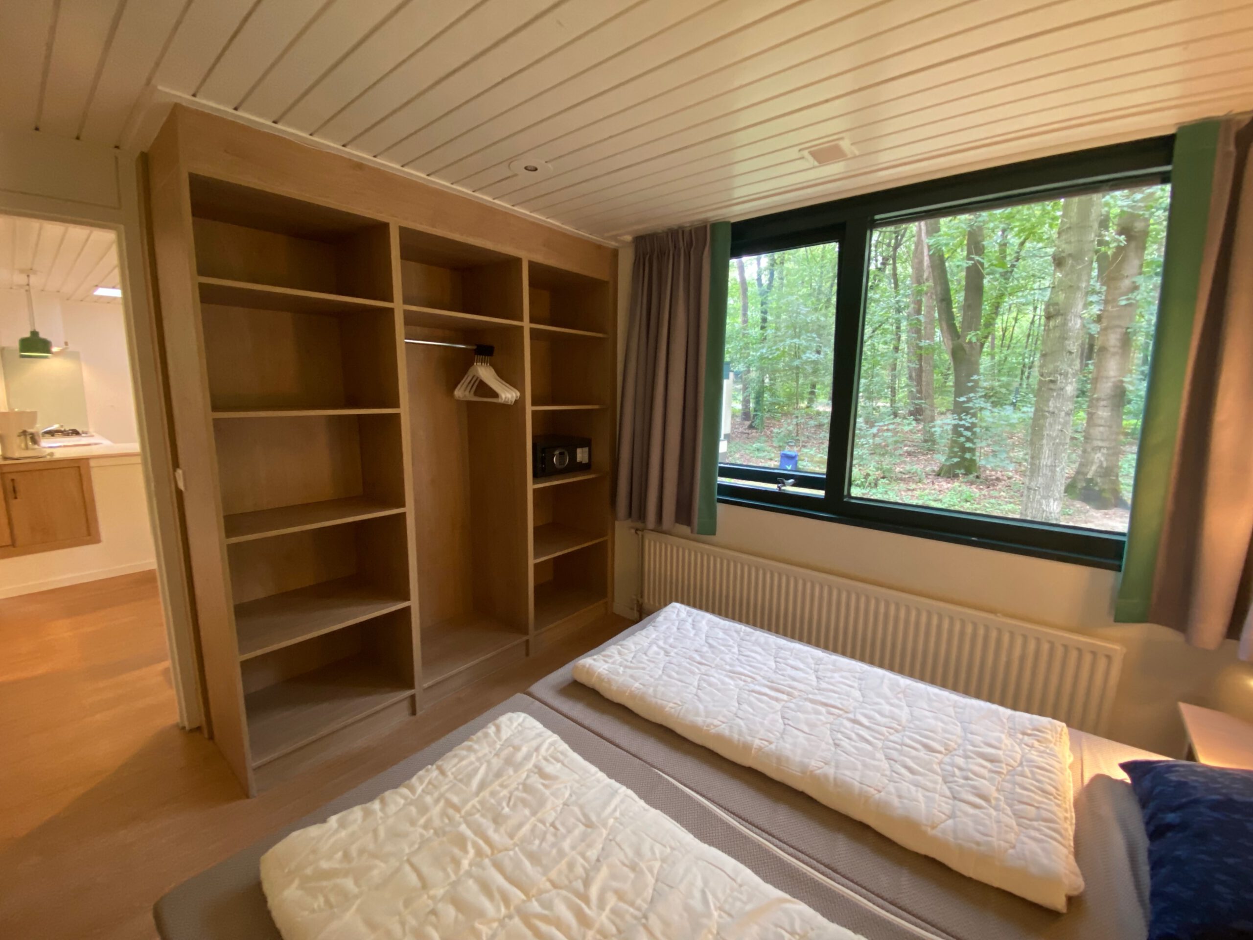 Bedroom inside Center Parcs Het Heijderbos 4 pers. Premium HB1922 cottage 965, featuring twin beds, large wardrobe with built in safe, open shelving and forest view from the window.