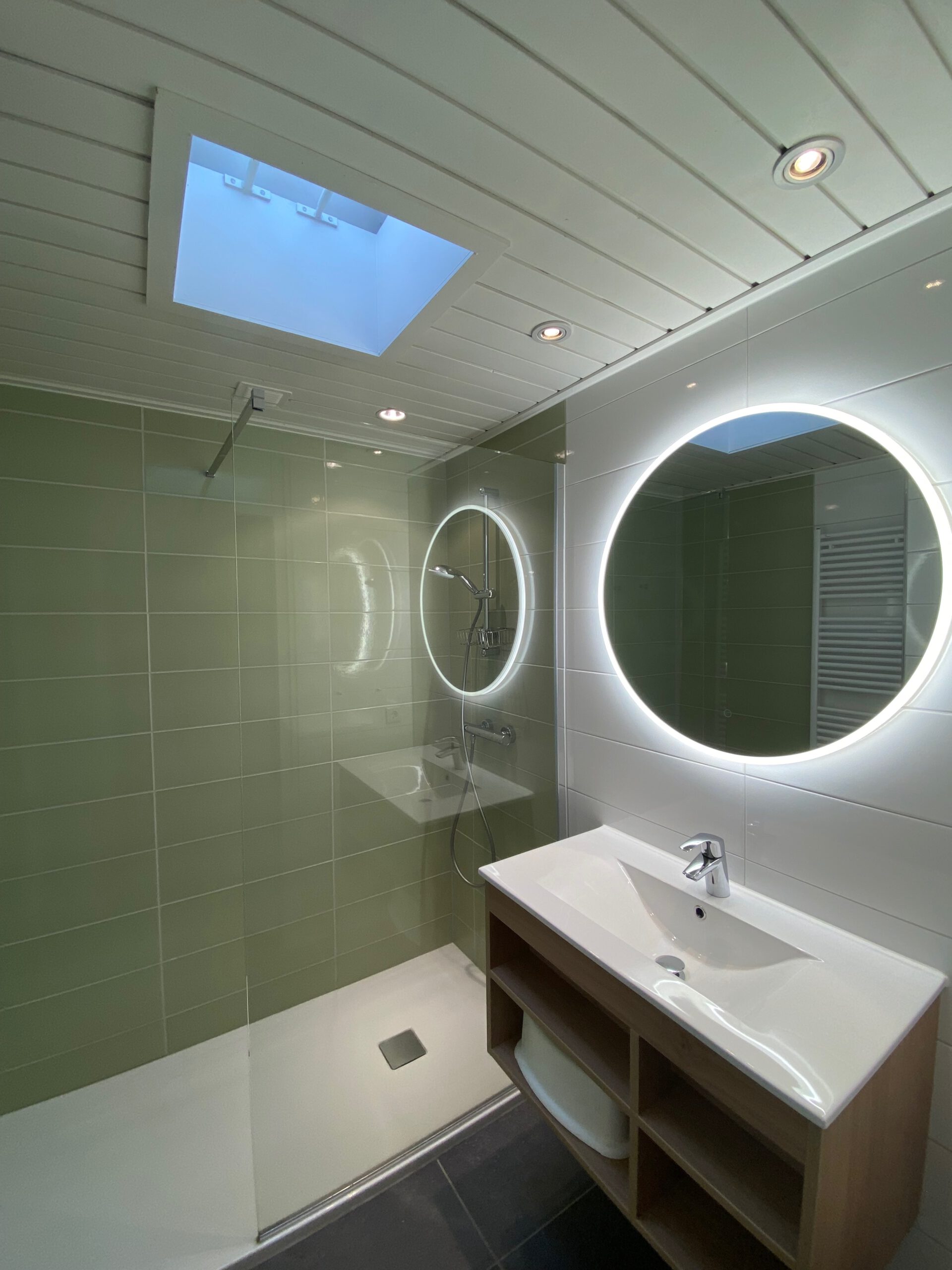 Modern bathroom inside Center Parcs Het Heijderbos 4 pers. Premium HB1922 cottage 965 featuring walk in shower, illuminated round mirror, skylight and open storage under the sink.