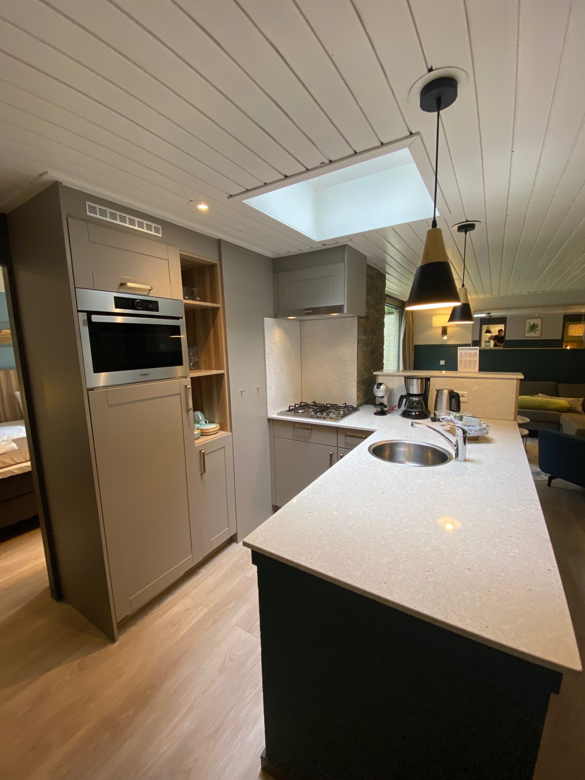 Spacious kitchen layout in Center Parcs Het Heijderbos VIP cottage 978 with skylight, gas cooktop, built in combi microwave, sink, Dolce Gusto machine, filter coffee maker, and luxury countertop with natural stone details.