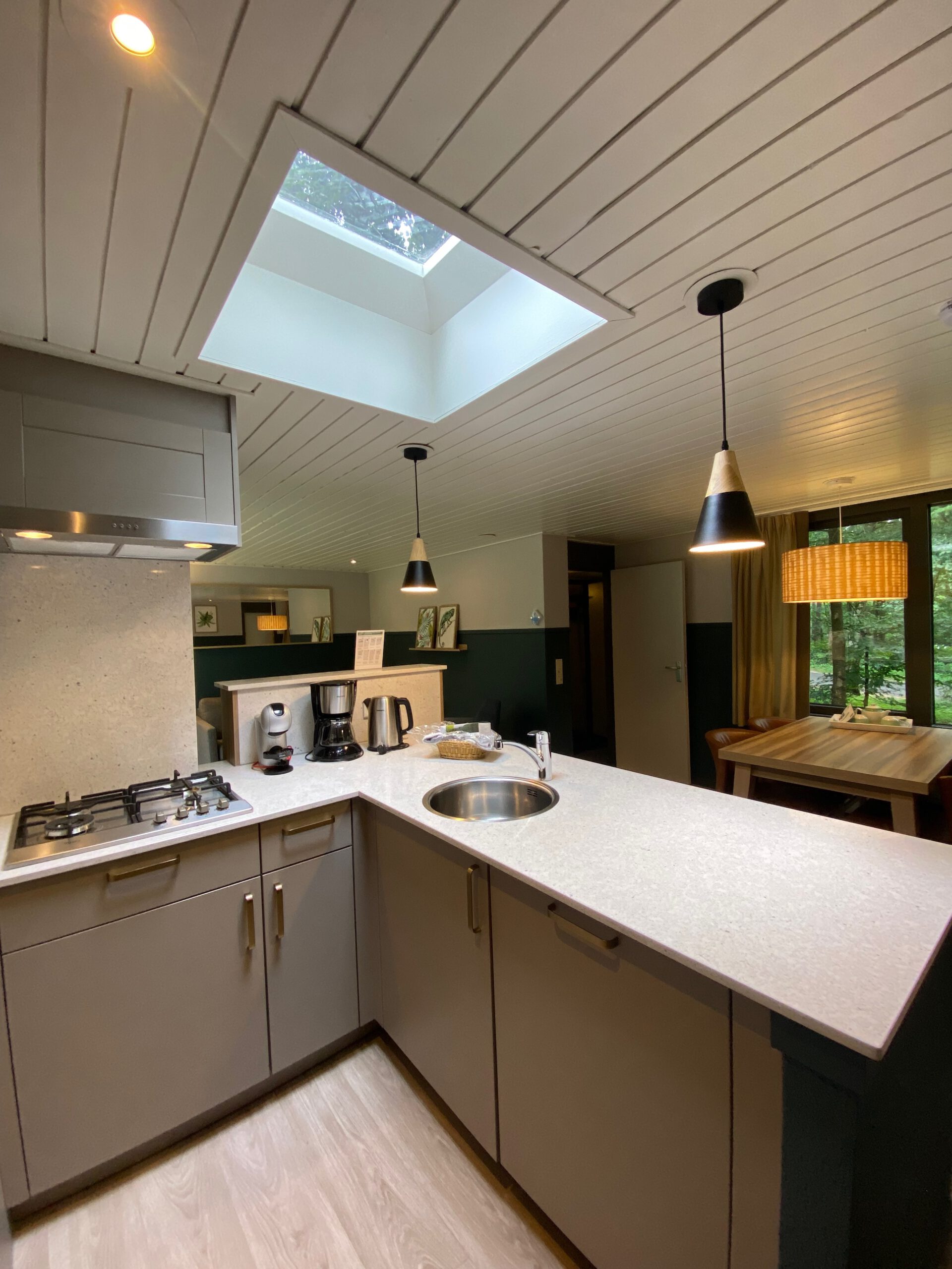 Modern open kitchen inside Center Parcs Het Heijderbos VIP cottage 978, featuring a gas stove with extractor hood, combi microwave oven, Dolce Gusto coffee machine, filter coffee maker, kettle, fridge freezer combination, toaster, and natural stone wall finish.