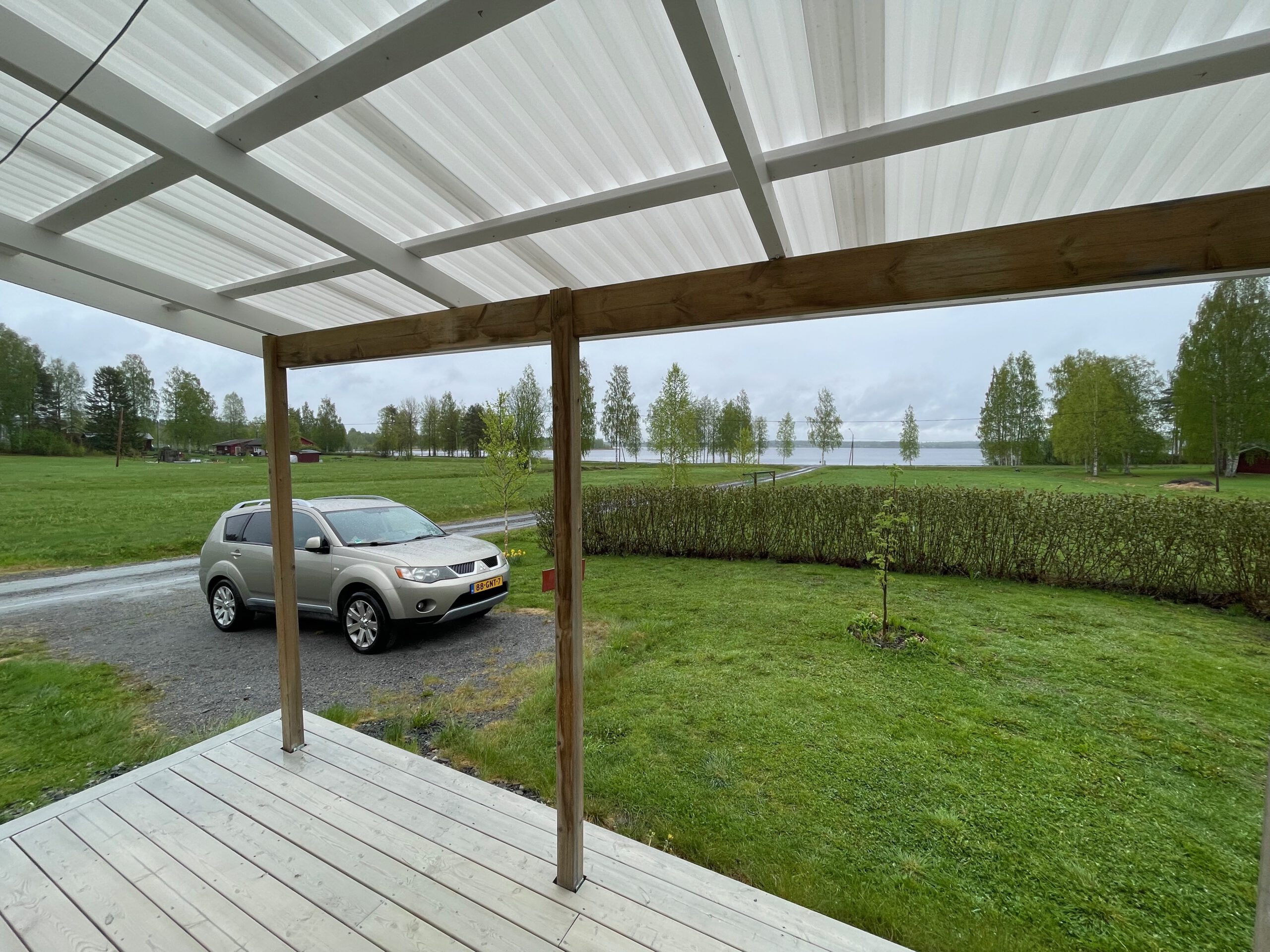 Cozy cottage with lake view Norra bergfors, covered porch view with green meadow, private parking where Timobiel is standing (Mitsubishi Outlander) and Lake Varuträsket in rural Sweden