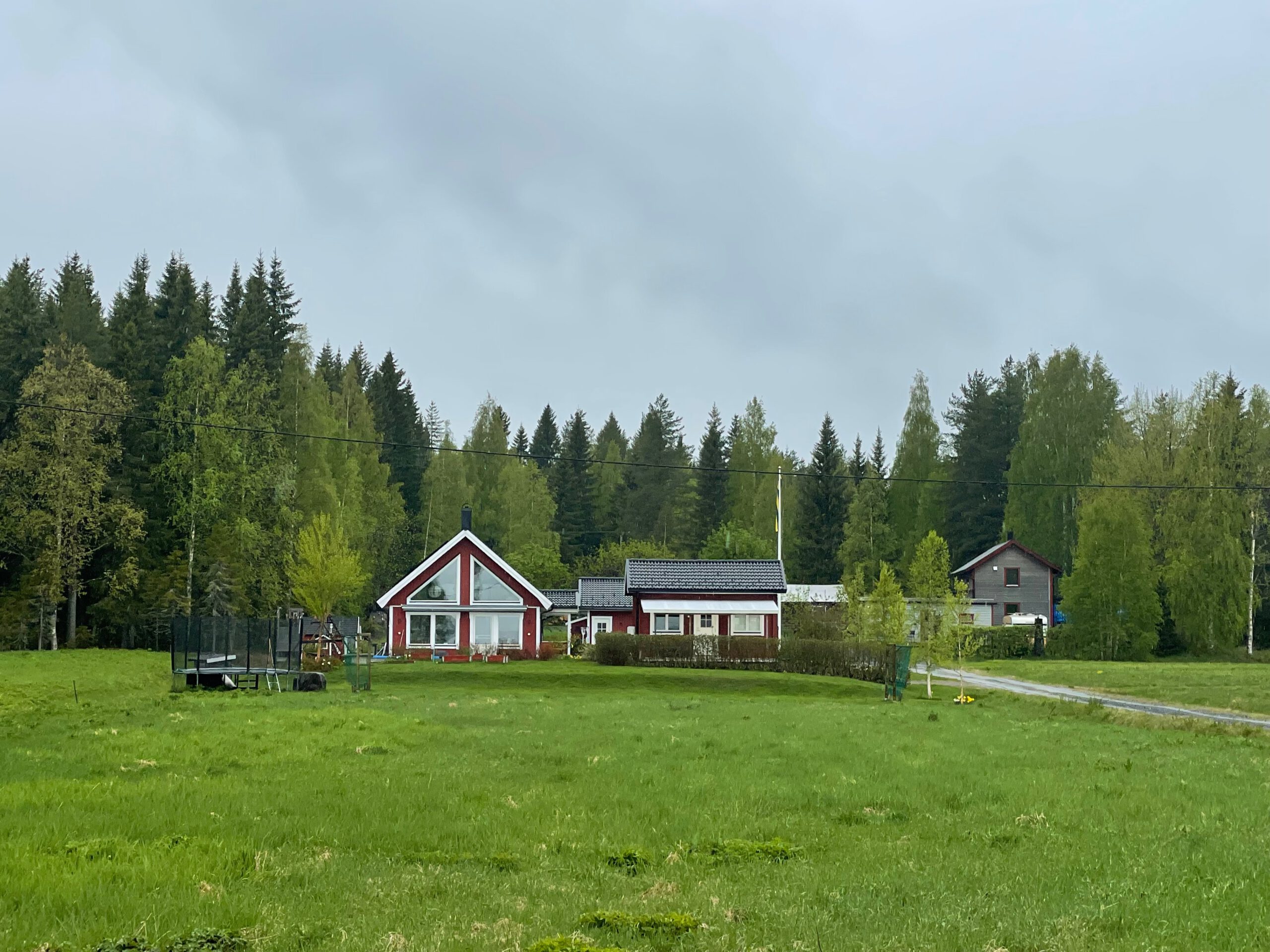 Cozy cottage with lake view Norra bergfors, owner’s main house on a rural Swedish property with green meadow, red wooden homes and forest surroundings