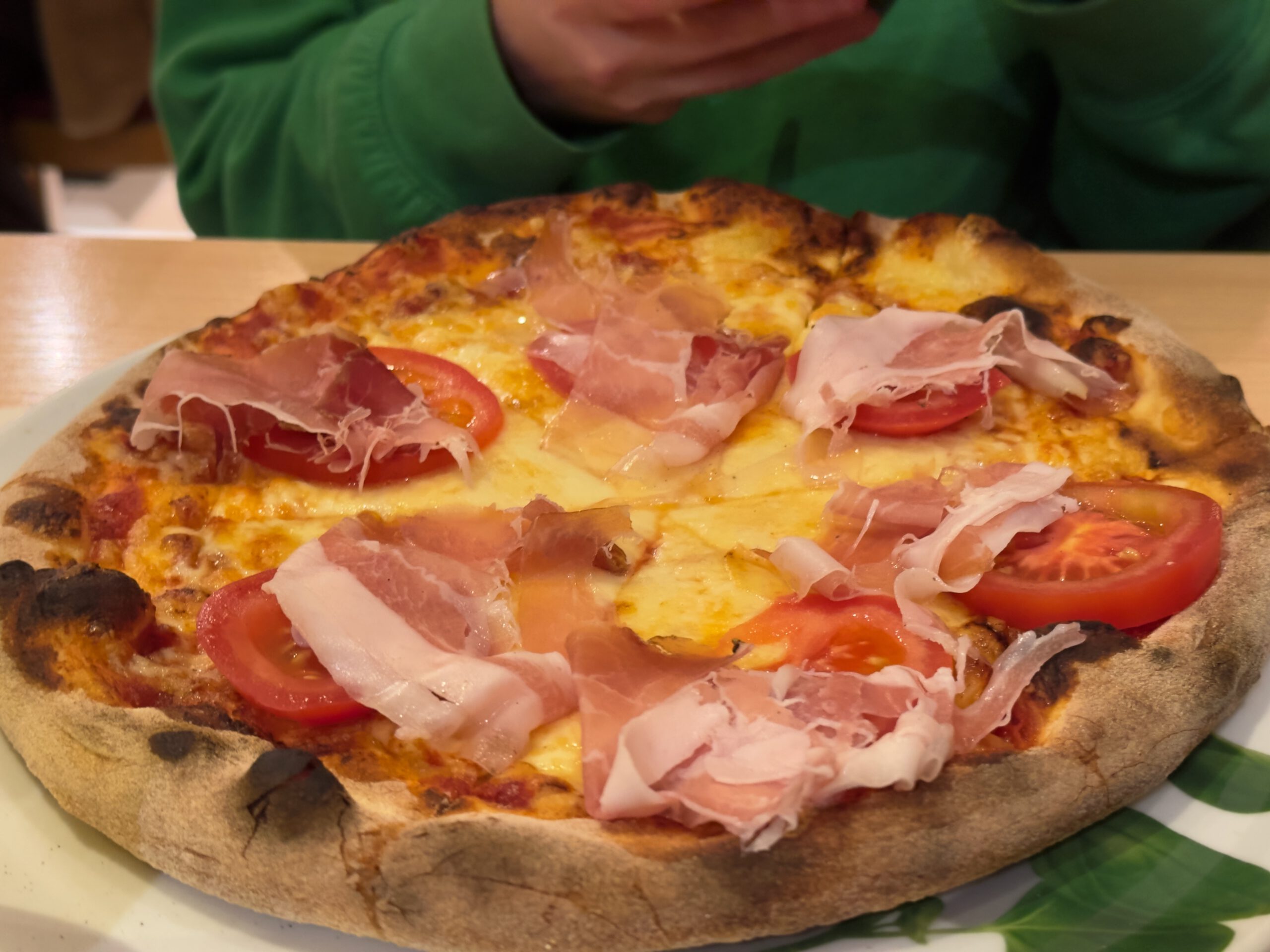 Pizzeria Il Genio Karken restaurant review featuring a freshly baked Italian pizza topped with melted mozzarella, sliced tomatoes, and thinly cut prosciutto, served hot on a classic stone baked crust inside the restaurant.