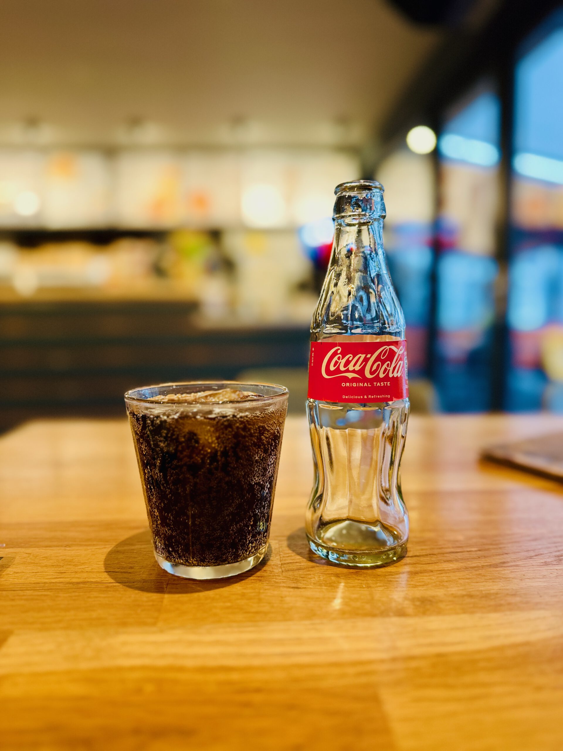 Verhage Burgh Haamstede Coca Cola bottle and glass of cola on wooden table inside the restaurant, refreshing soft drink served during dinner with blurred counter and menu boards in the background in Burgh Haamstede, Netherlands.