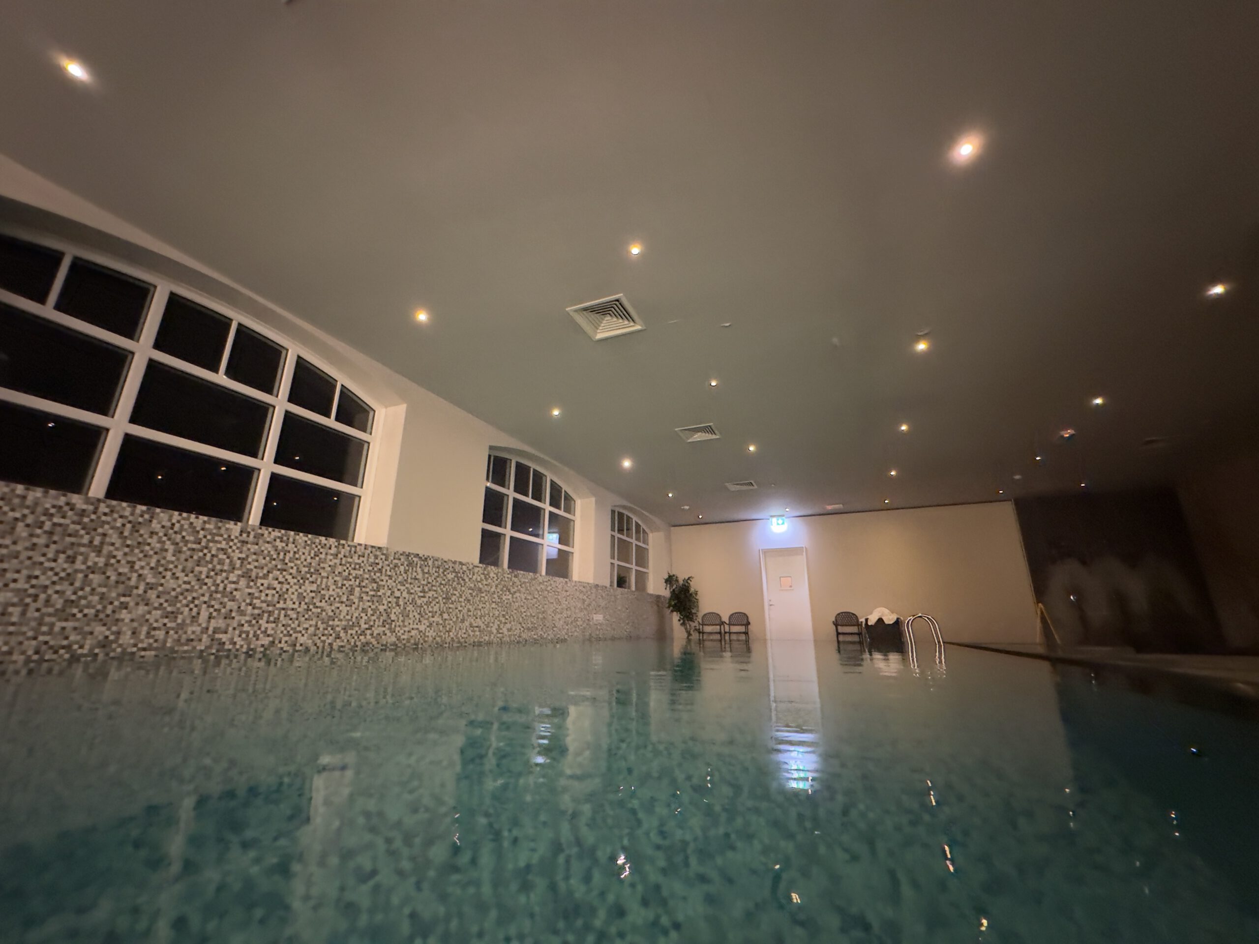 Grand Hotel Ter Duin spa review – indoor swimming pool at night with calm water reflections, mosaic tile walls and warm ceiling lighting in the wellness area.