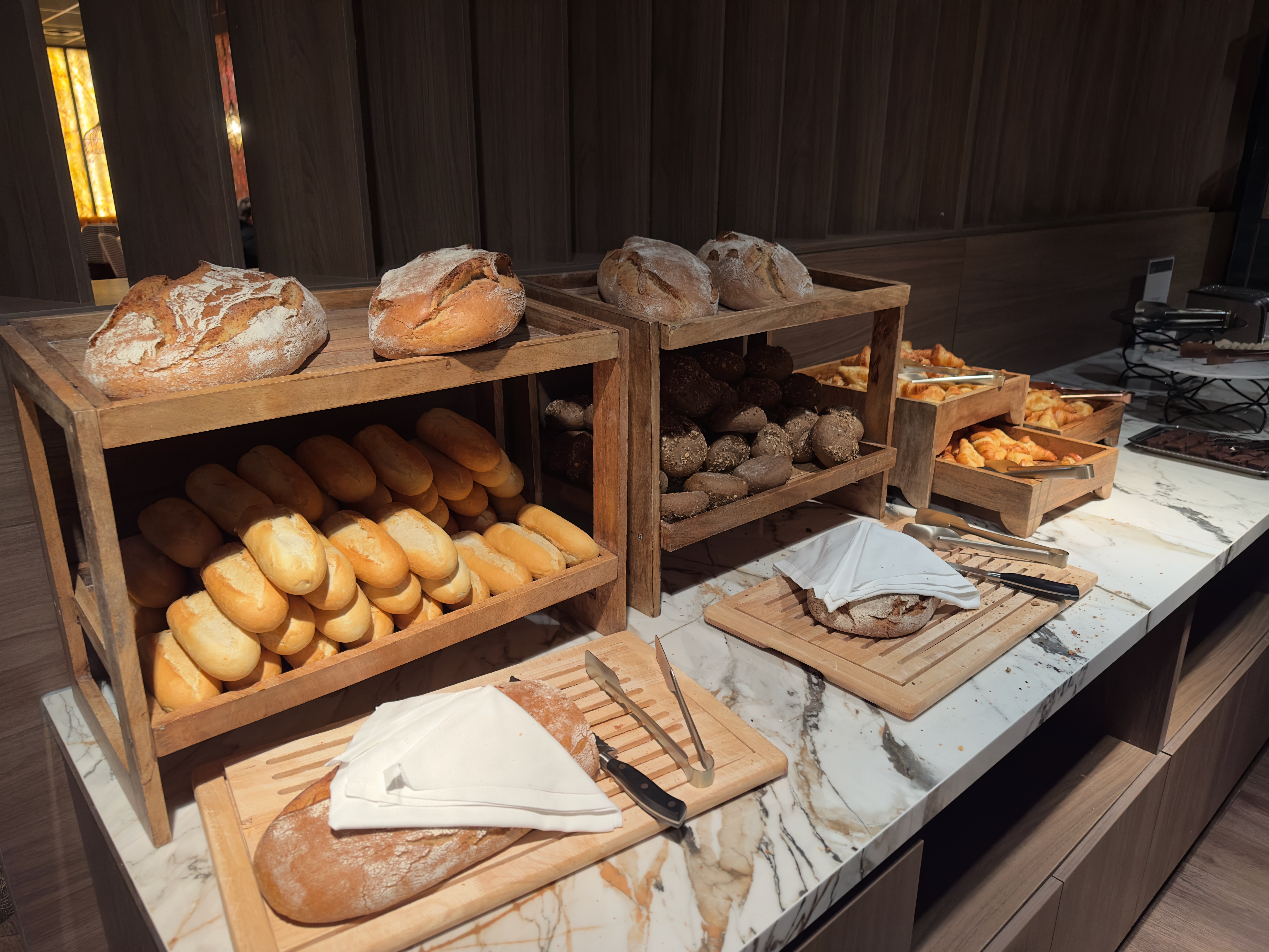 Grand Hotel Ter Duin review – fresh artisan bread selection at the breakfast buffet including white rolls, multigrain rolls and rustic loaves displayed in wooden crates on a marble counter in the hotel restaurant.