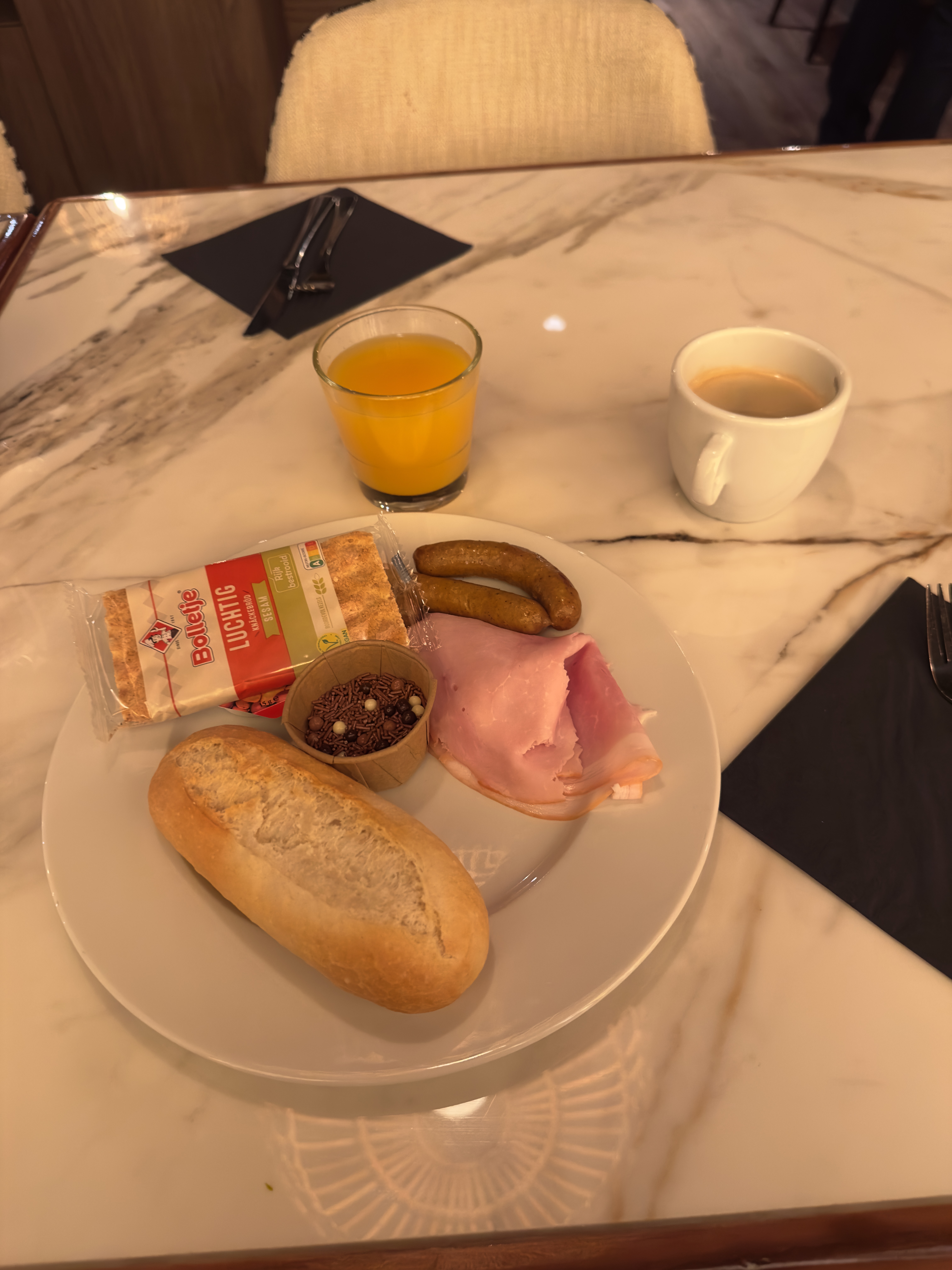 Grand Hotel Ter Duin review – breakfast plate with fresh bread roll, ham, cheese, chocolate sprinkles, sausages, orange juice and coffee served in the stylish hotel restaurant.